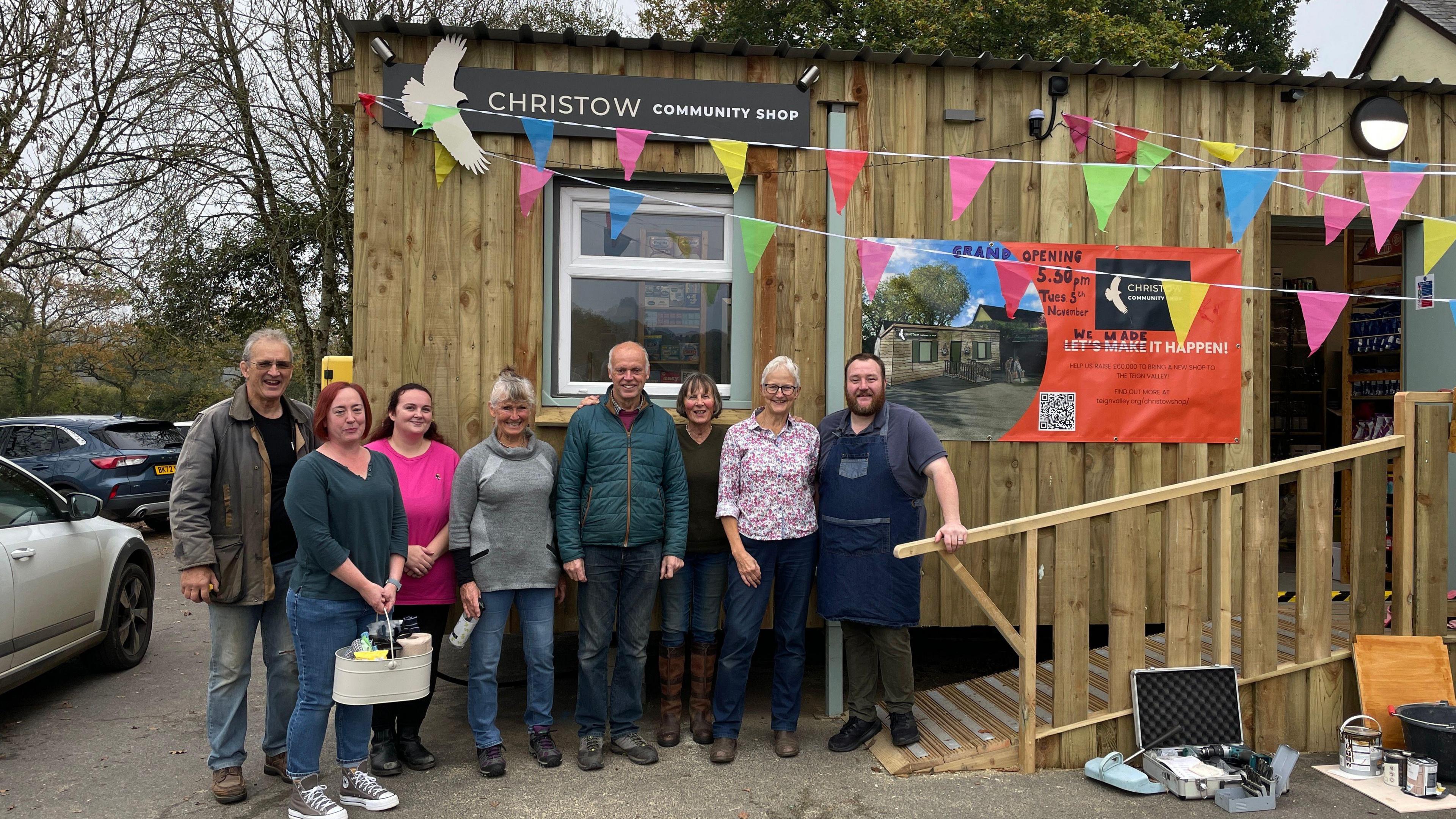 Volunteers and members of the team stood in a line infront of the shop which is clad in wood. 