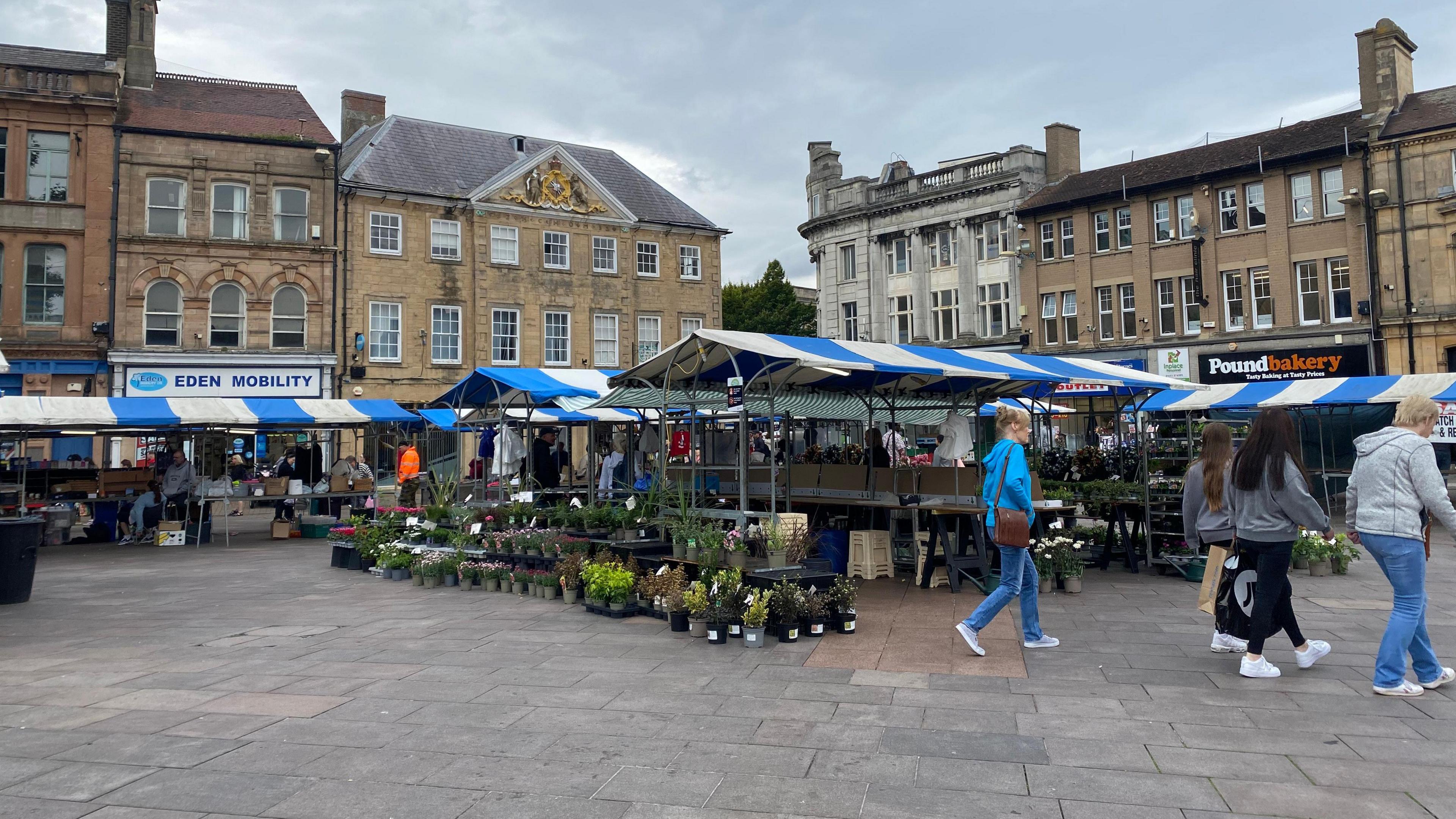 Mansfield town market, with blue and white canopies over several outdoor market stalls and a handful of shoppers walking past.