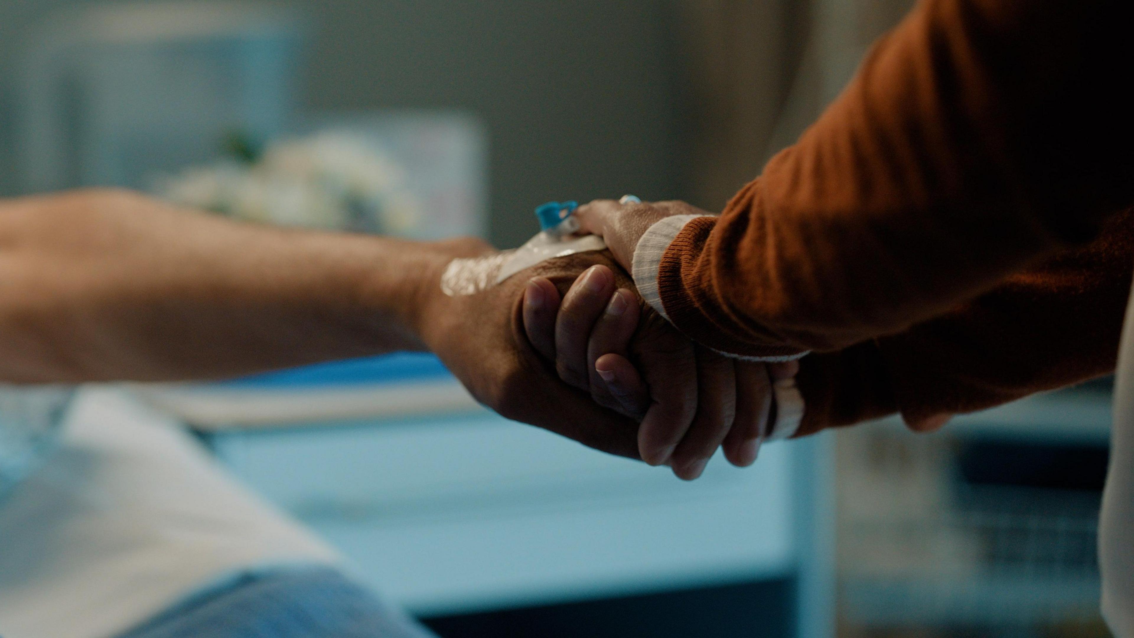 An image of two people holding hands in a hospital. 