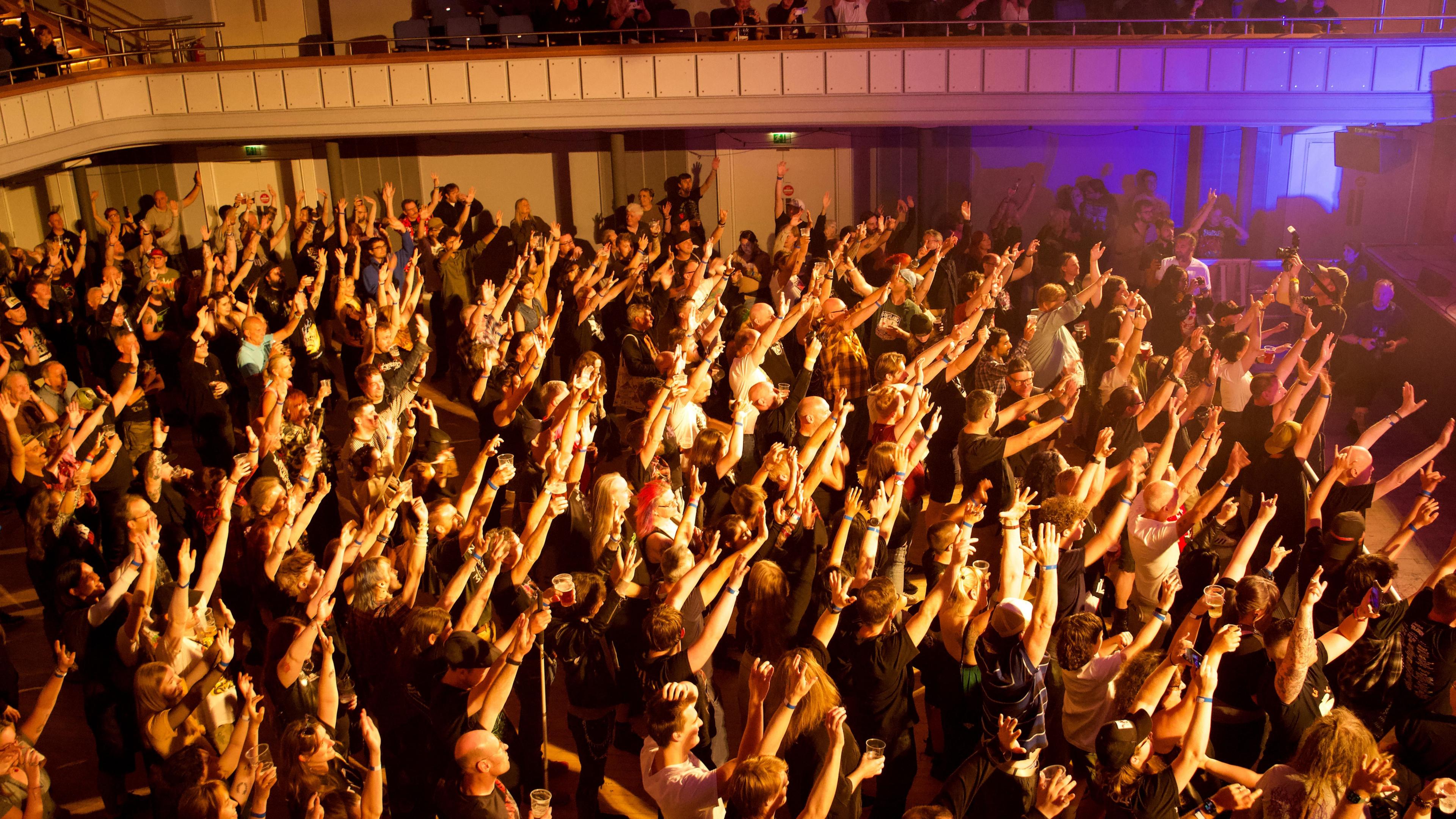 A large crowd of people stood in front of the Town Sall stage with their arms pointing upwards 