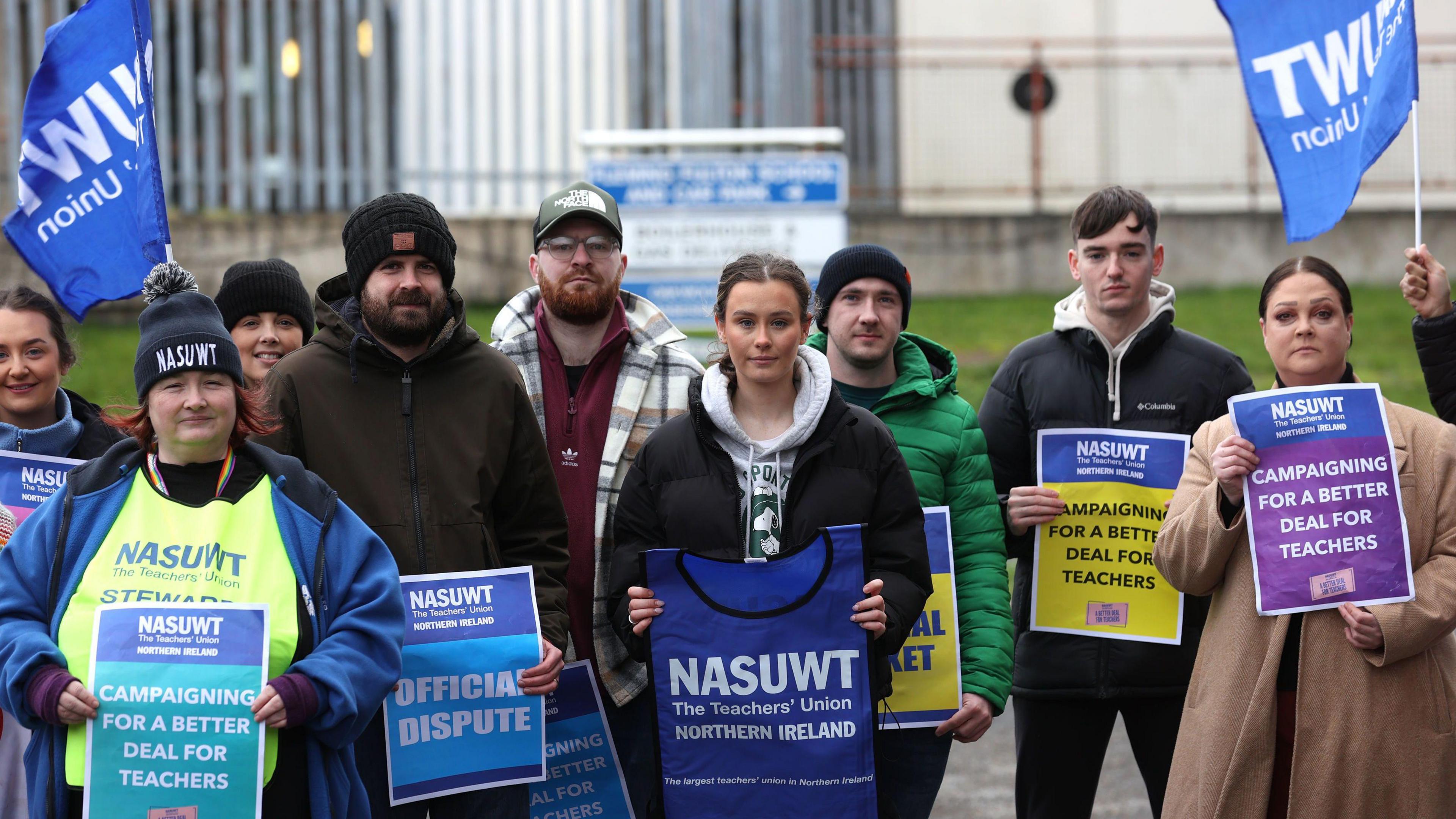 A number of people stand facing the camera. They're holding NASUWT branded signs.