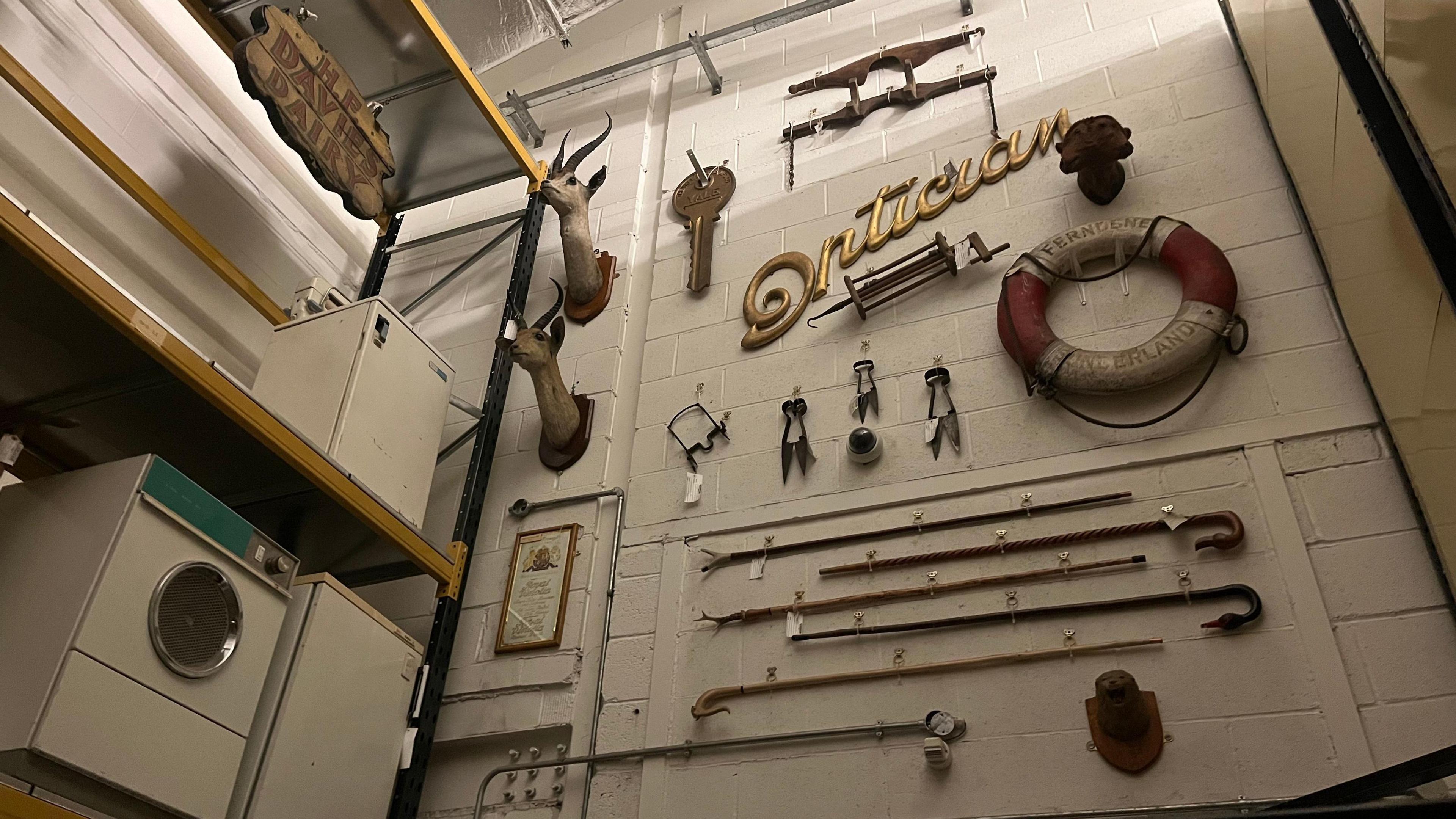 Wall covered with objects such as deer heads, a lifebuoy and walking sticks. It is next to a shelf holding a washing machine. 