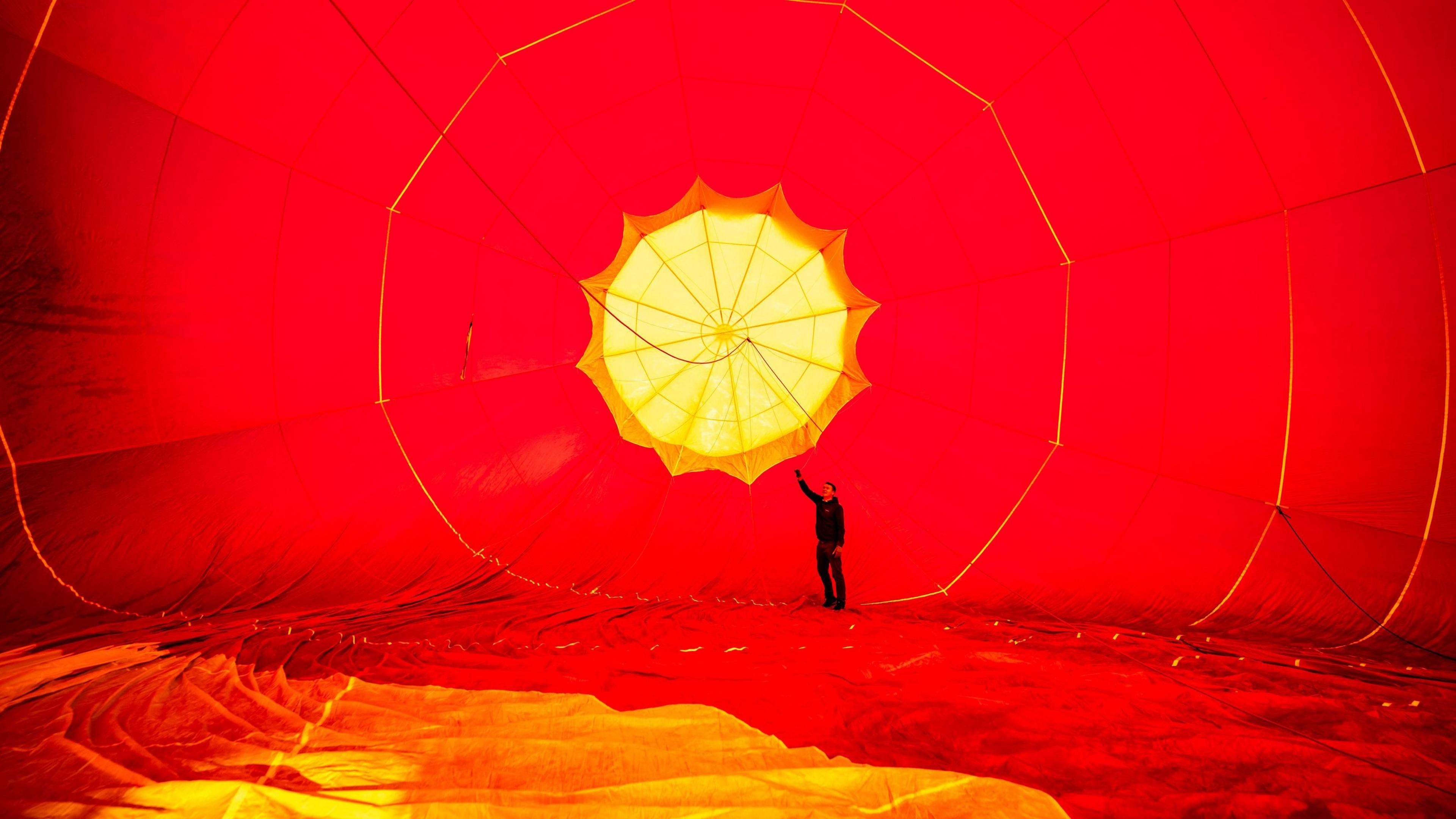 Inside of a red hot air ballon that has been partially inflated. A man stands at the far end.