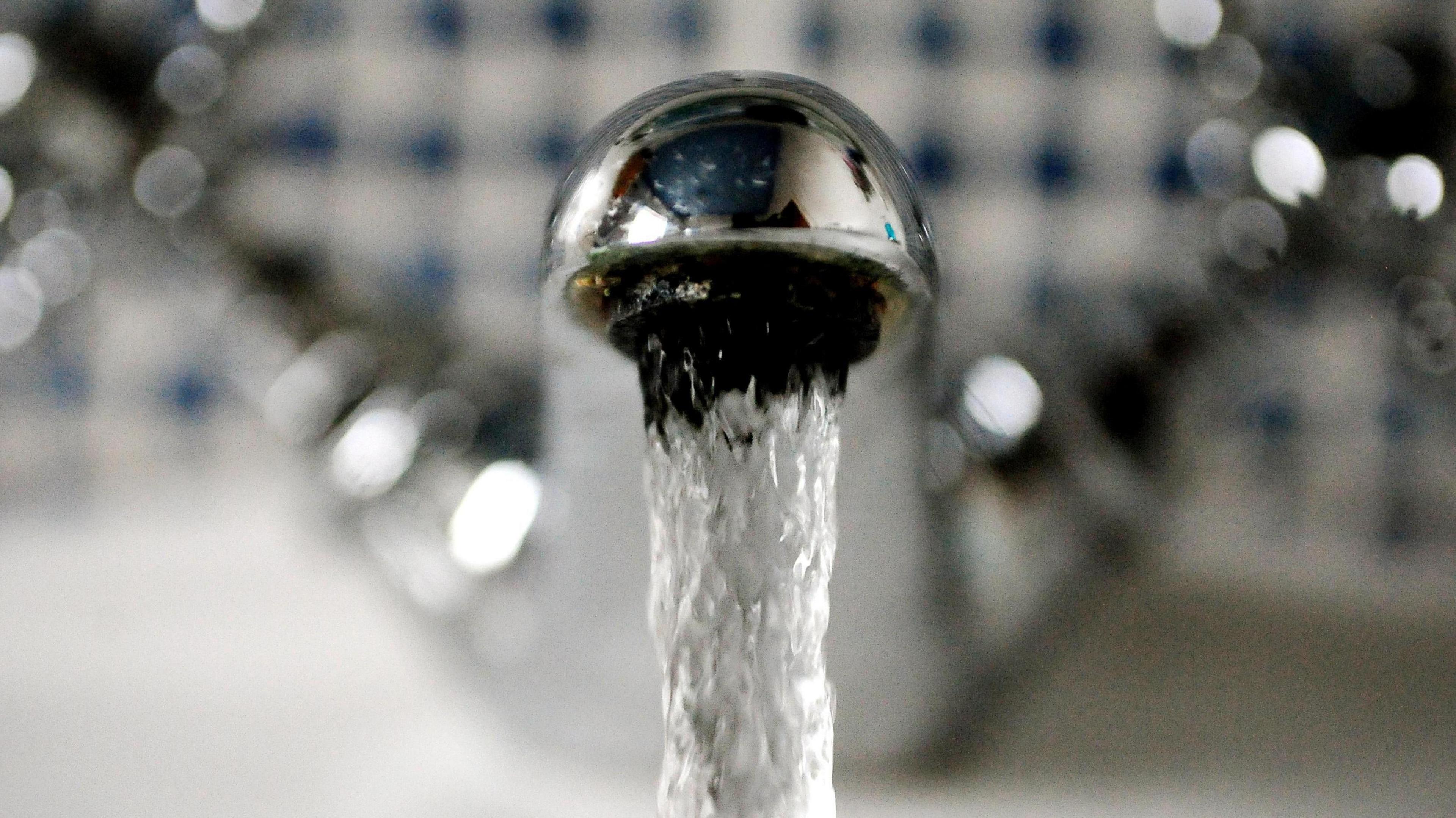 A close up of a silver tap with running water coming out of it.