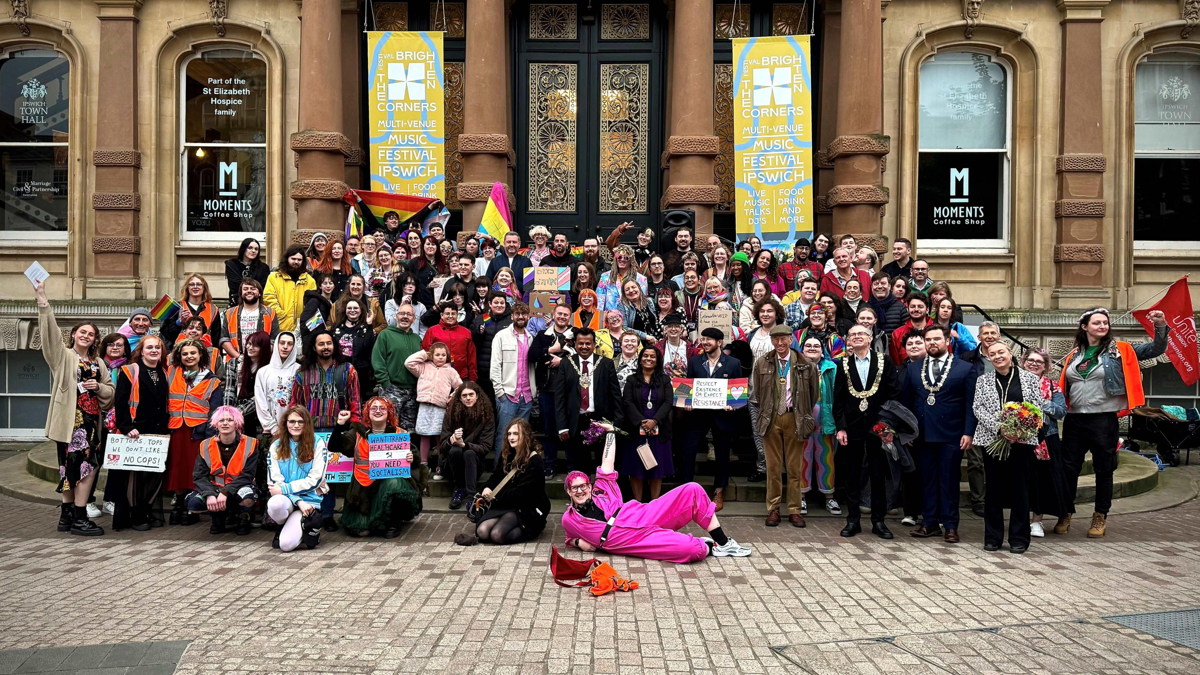 A large crowd on the steps of Ipswich Town Hall posing for a group photograph. One man lies at the front of the group wearing a pink boiler suit.