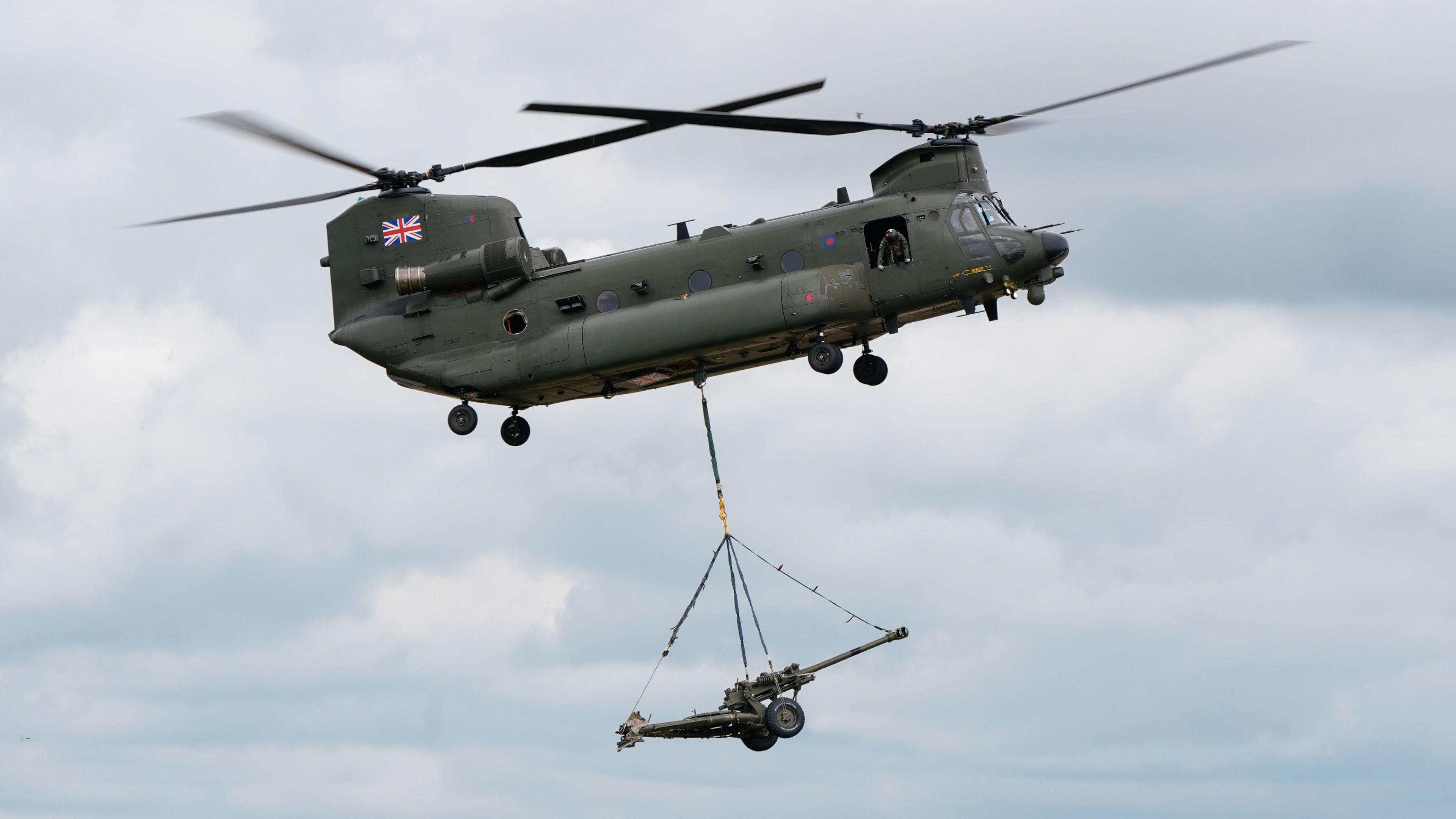 A helicopter is in the sky demonstrating its capabilities at an air show. It is a military helicopter in grey with the British flag on it.