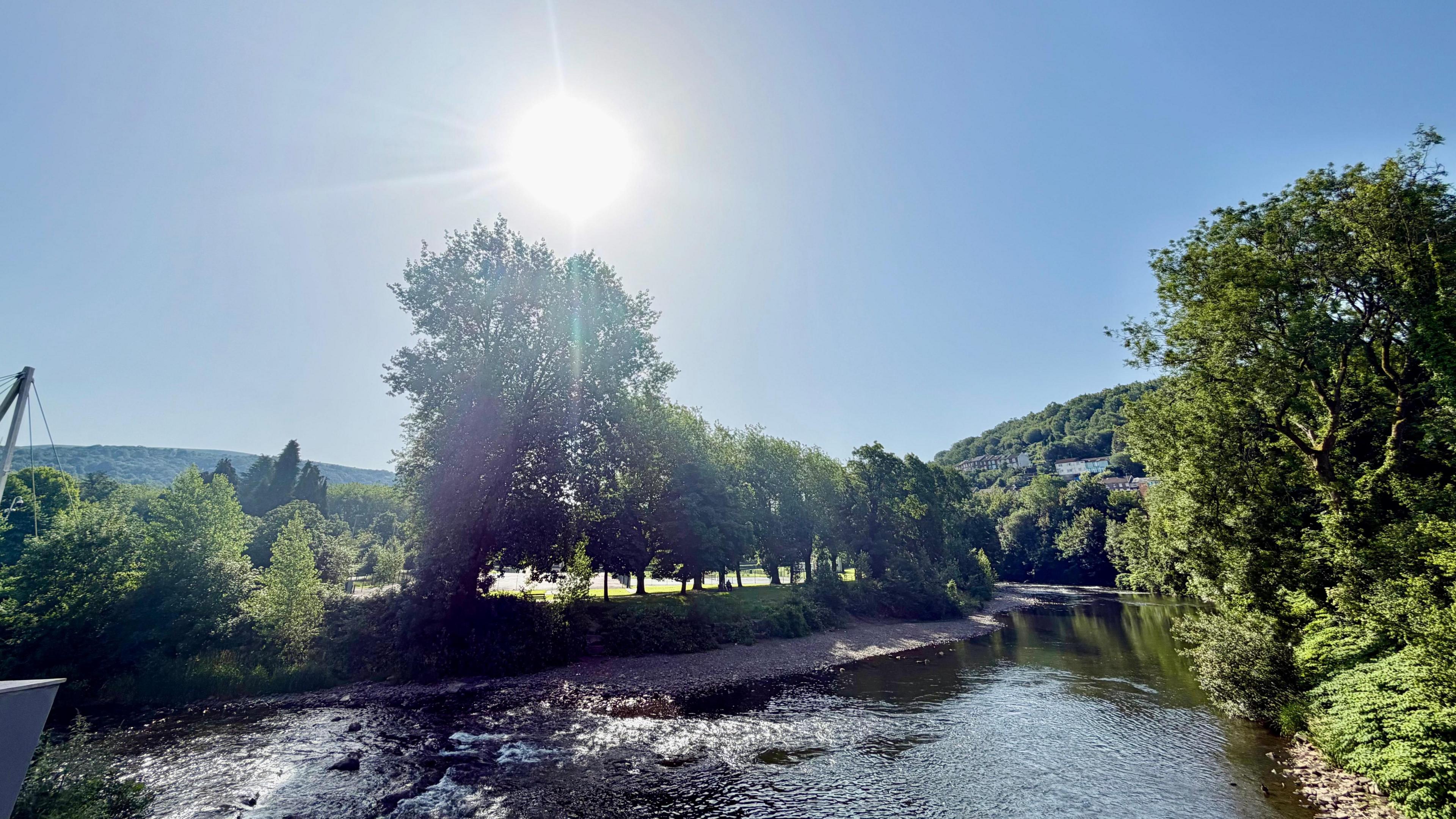 A sun low in the sky over a river bend. Trees line the river banks.