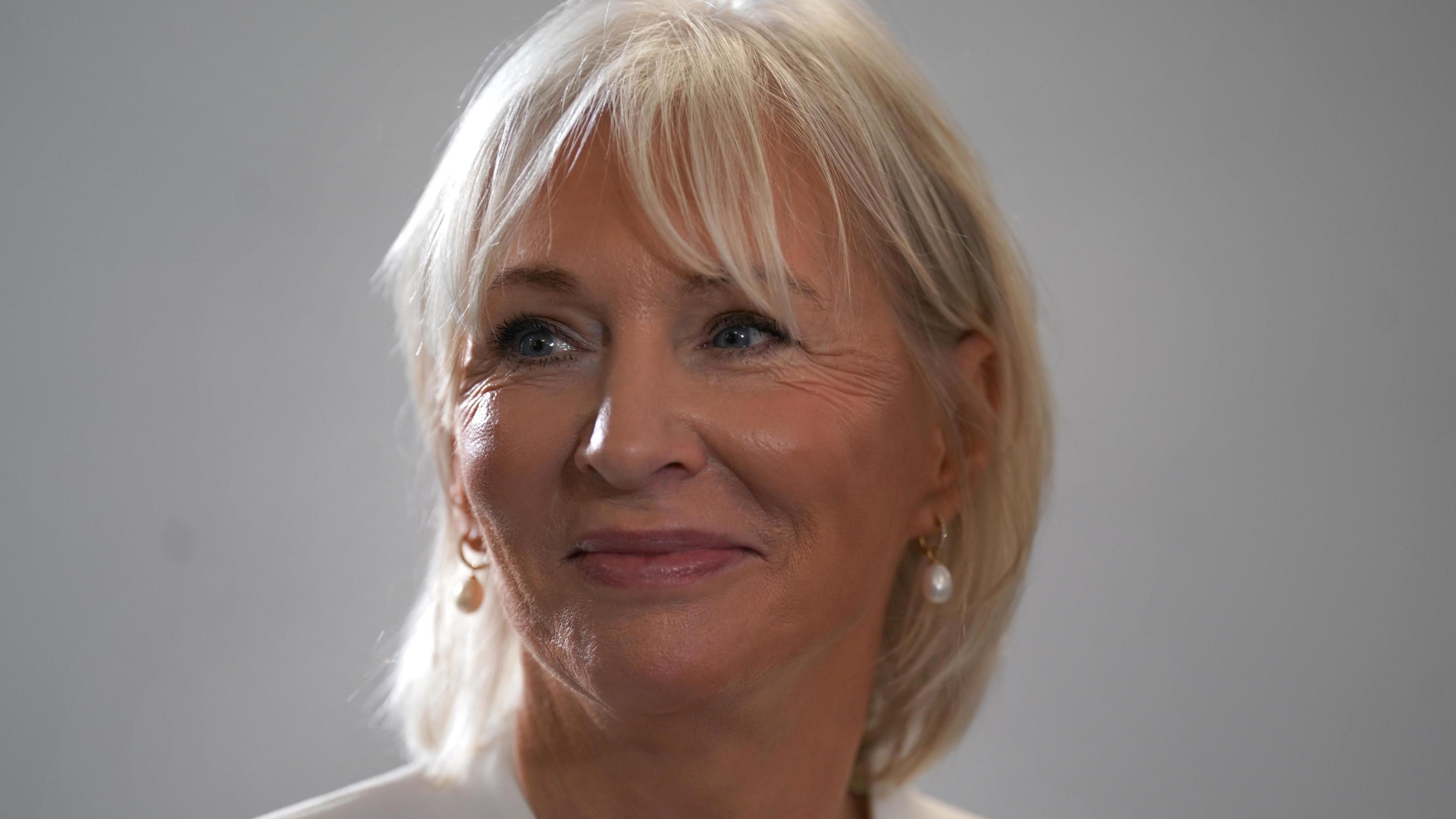 Nadine Dorries, who has short light blonde hair with a fringe and wears a white blazer, looks on at an event