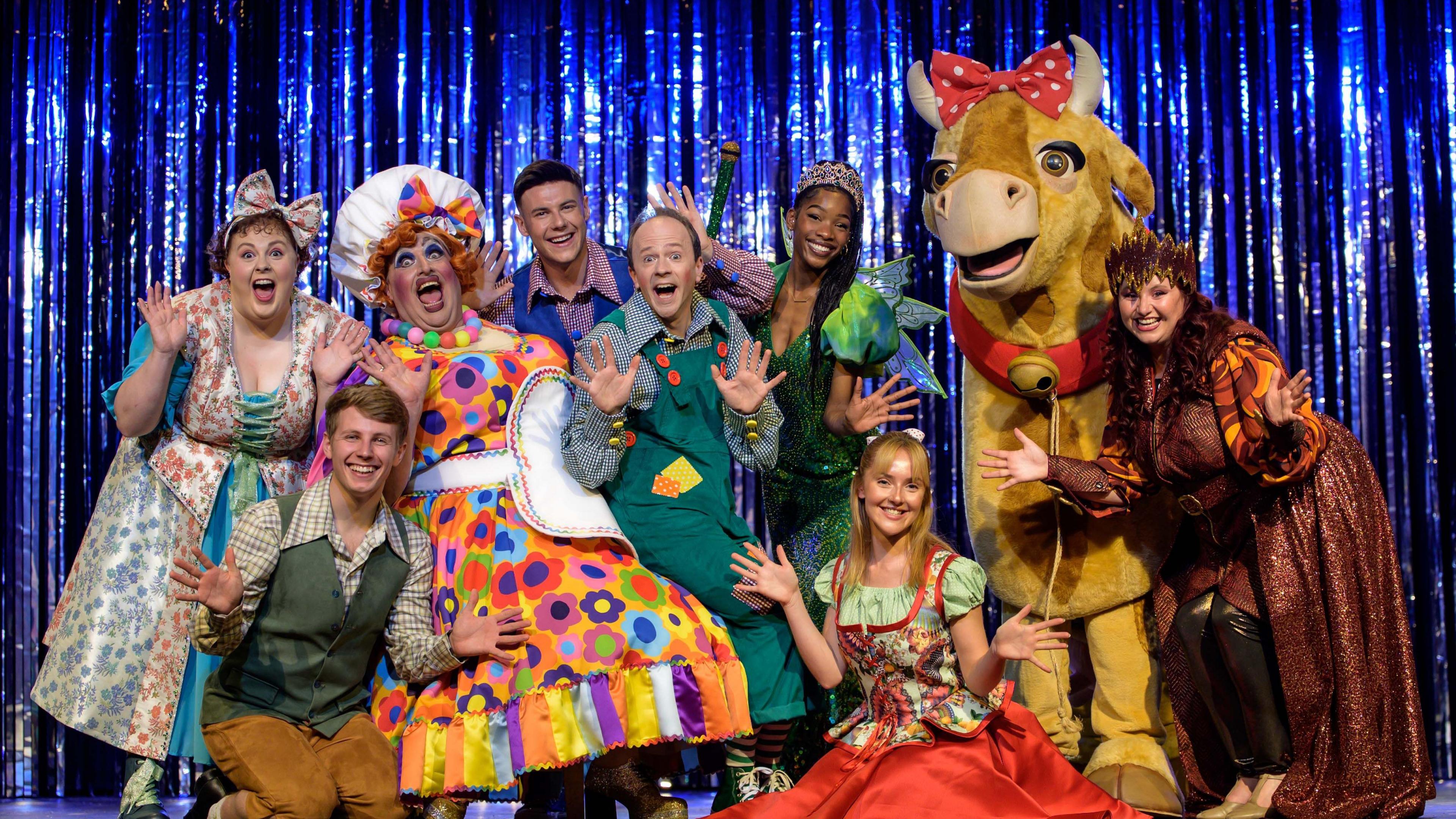 Pantomime performers smile at the camera on the stage of the Octagon Theatre