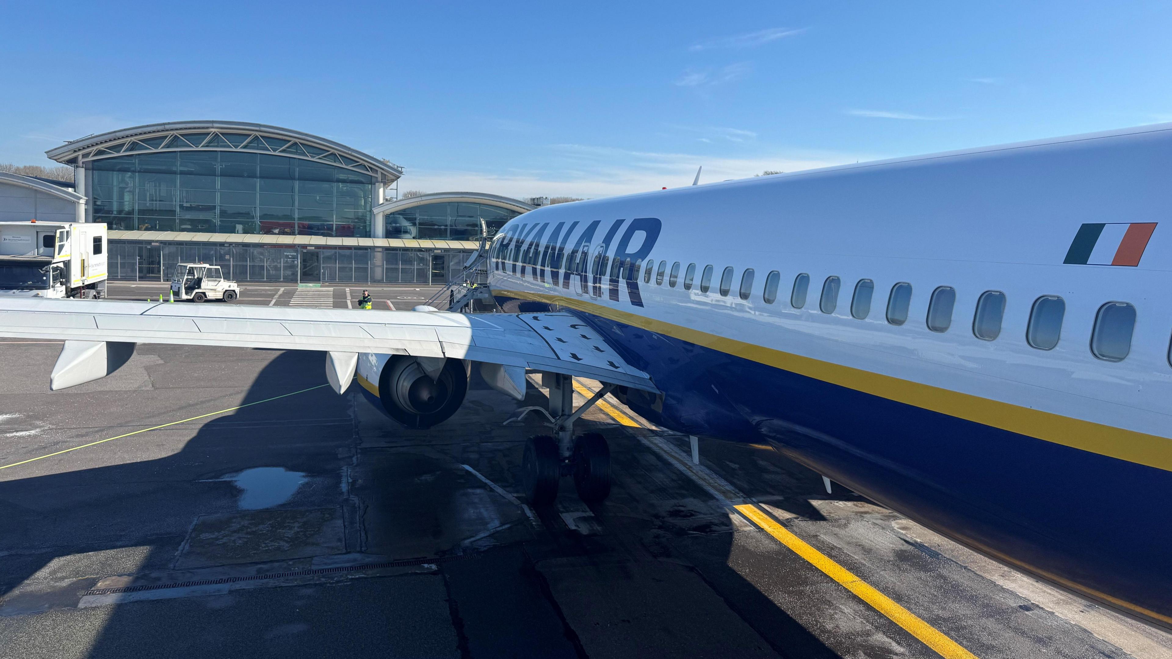 Ryanair passenger aircraft and wing viewed from the rear steps. The glass airport terminal is in the background.