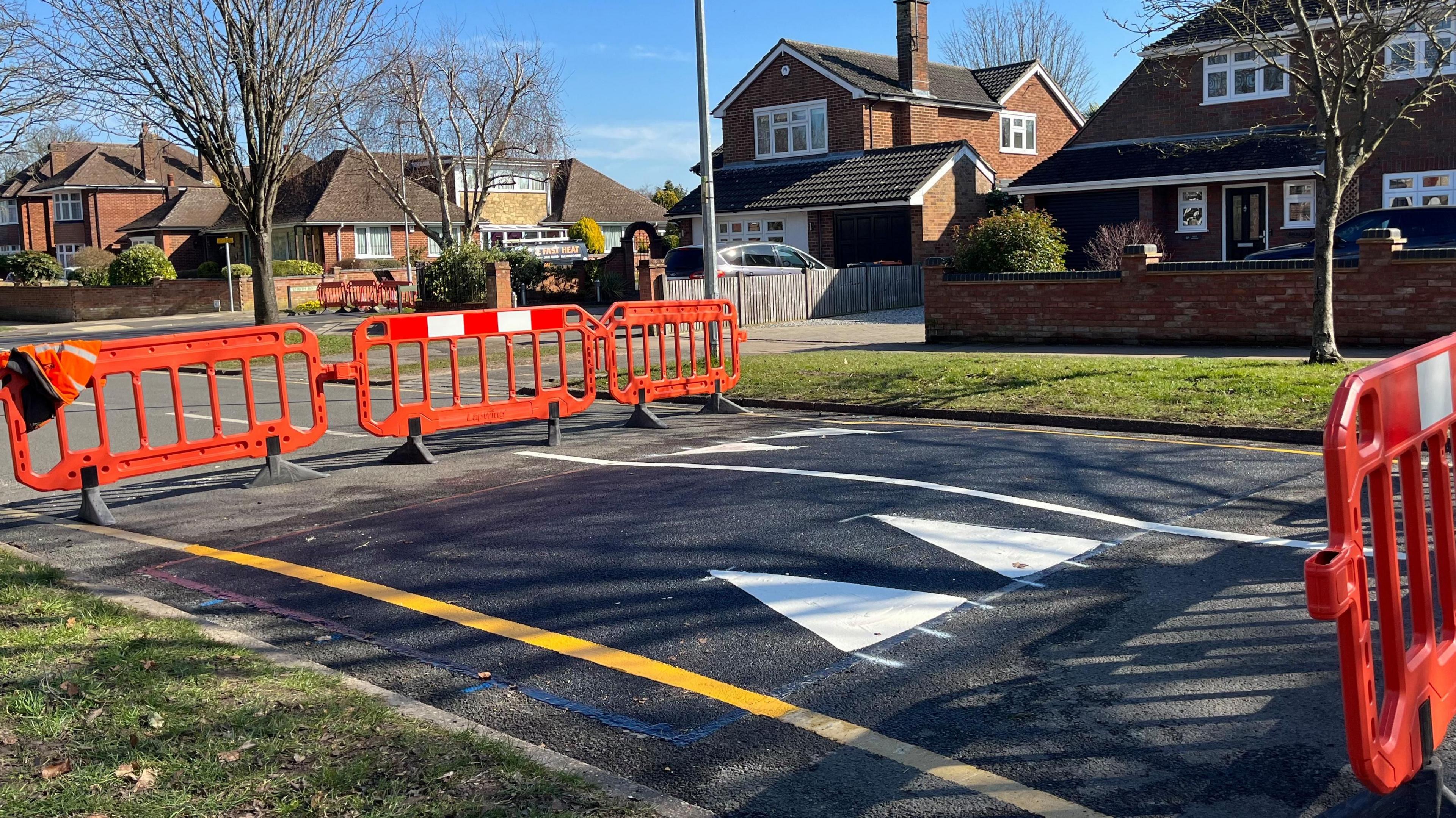 A newly installed speed hump on a road with barriers either side to protect the fresh paintwork and yellow lines.