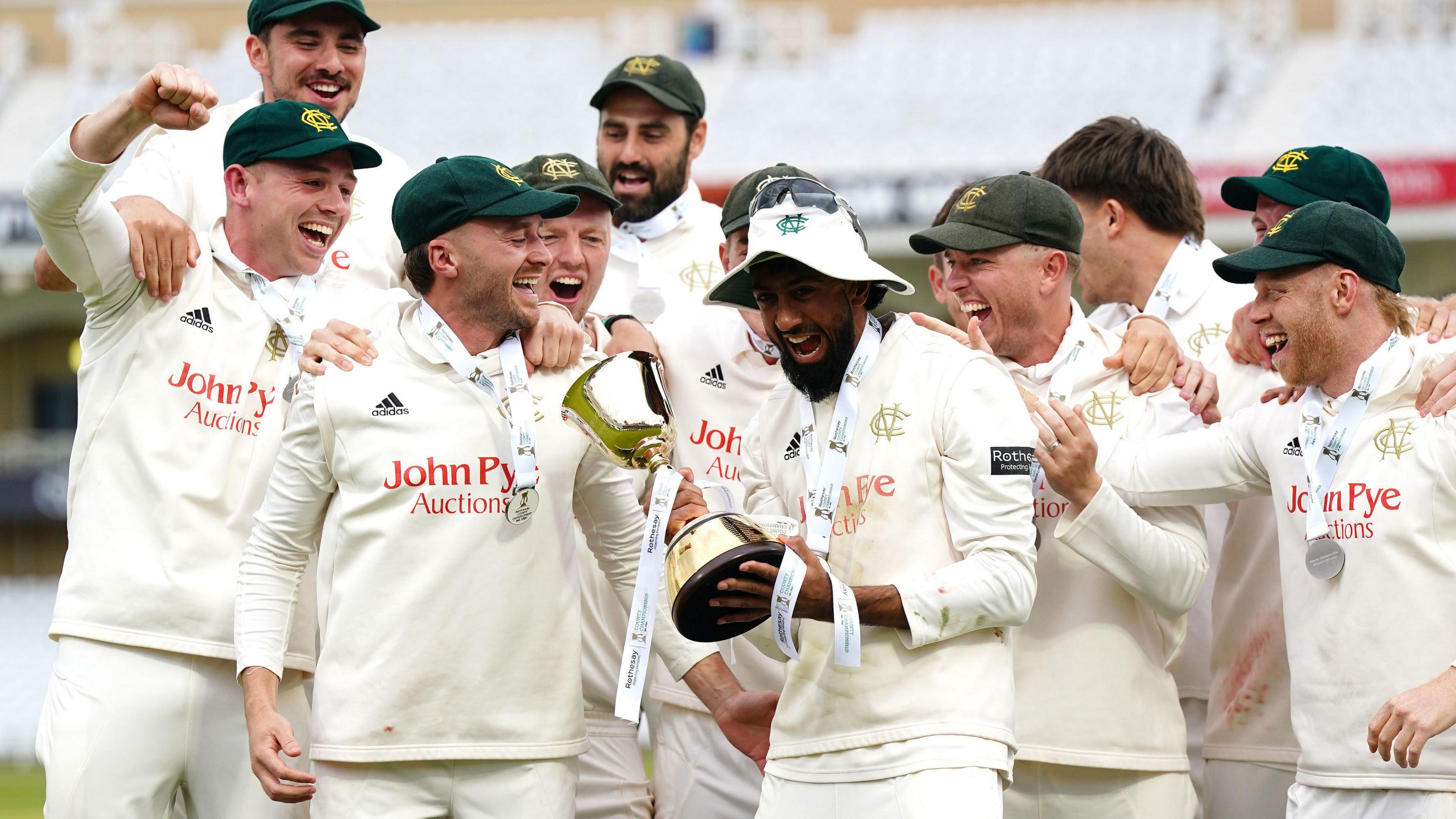 Nottinghamshire captain Haseeb Hameed holds the Division One trophy in both hands with a big smile on his face as the rest of his Nottinghamshire team-mates celebrate alongside him