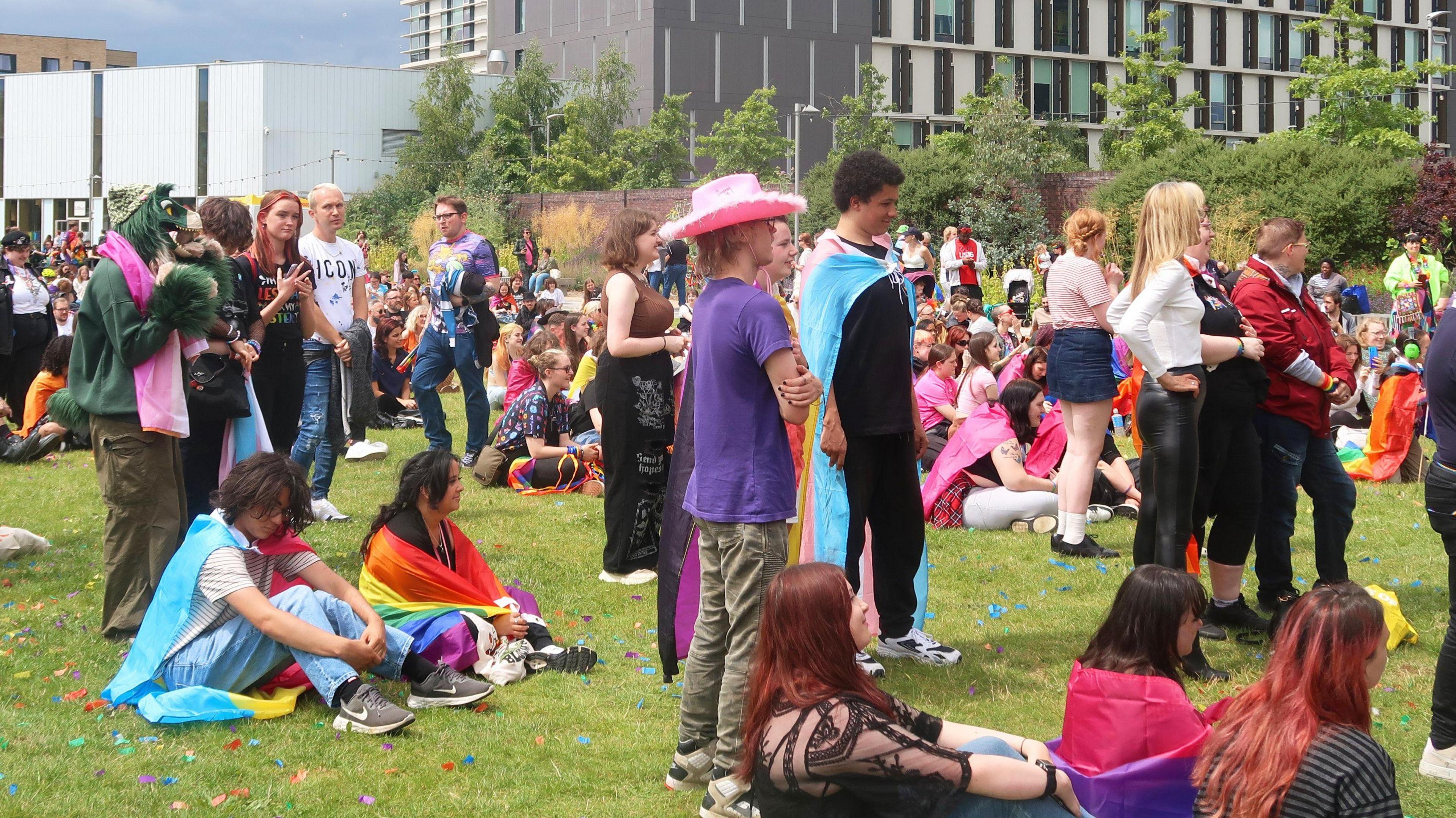 People of all ages, some in costume, sit or stand on grass