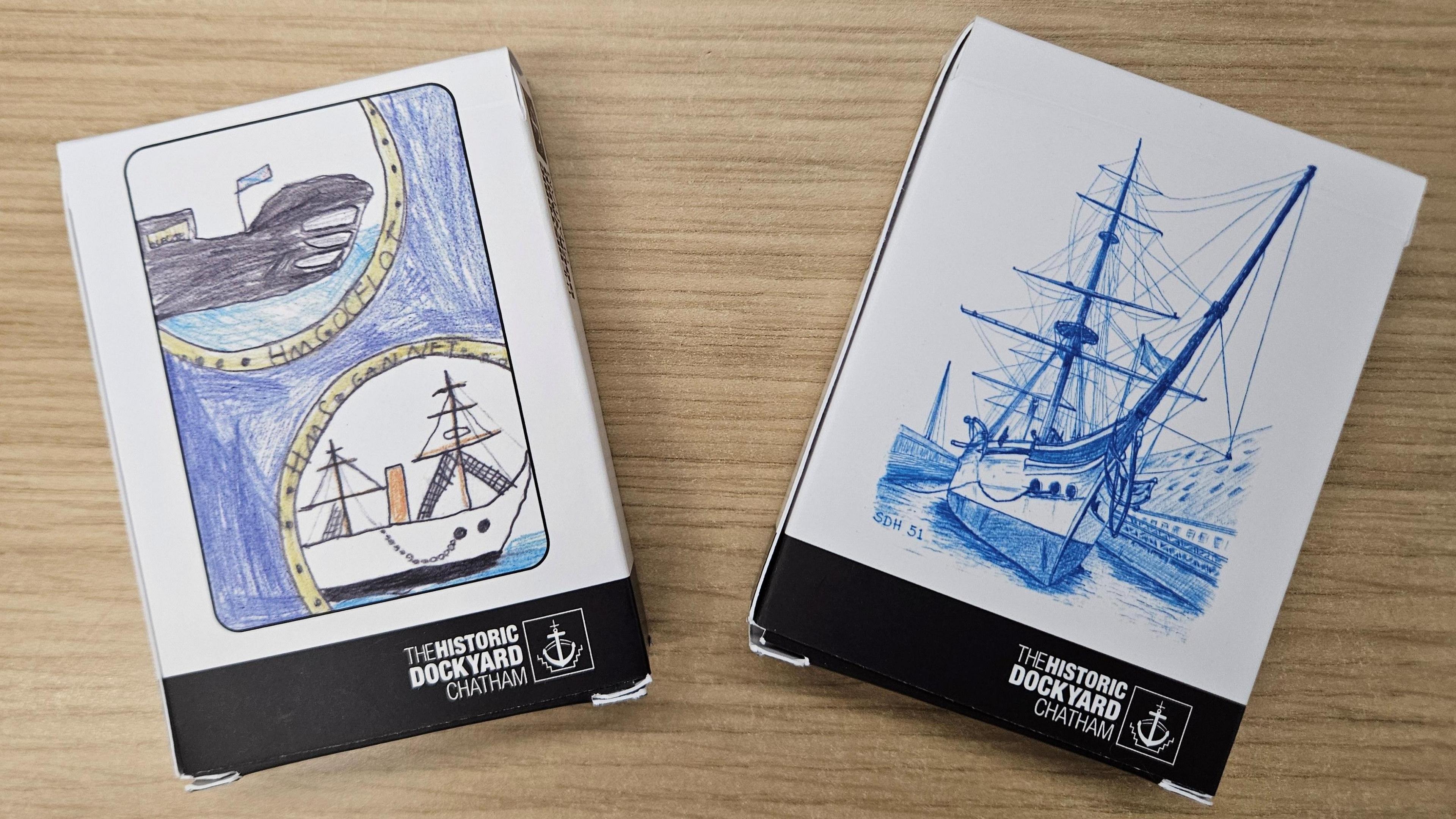 Two packs of playing cards lying on a table. Both have images of historical ships.