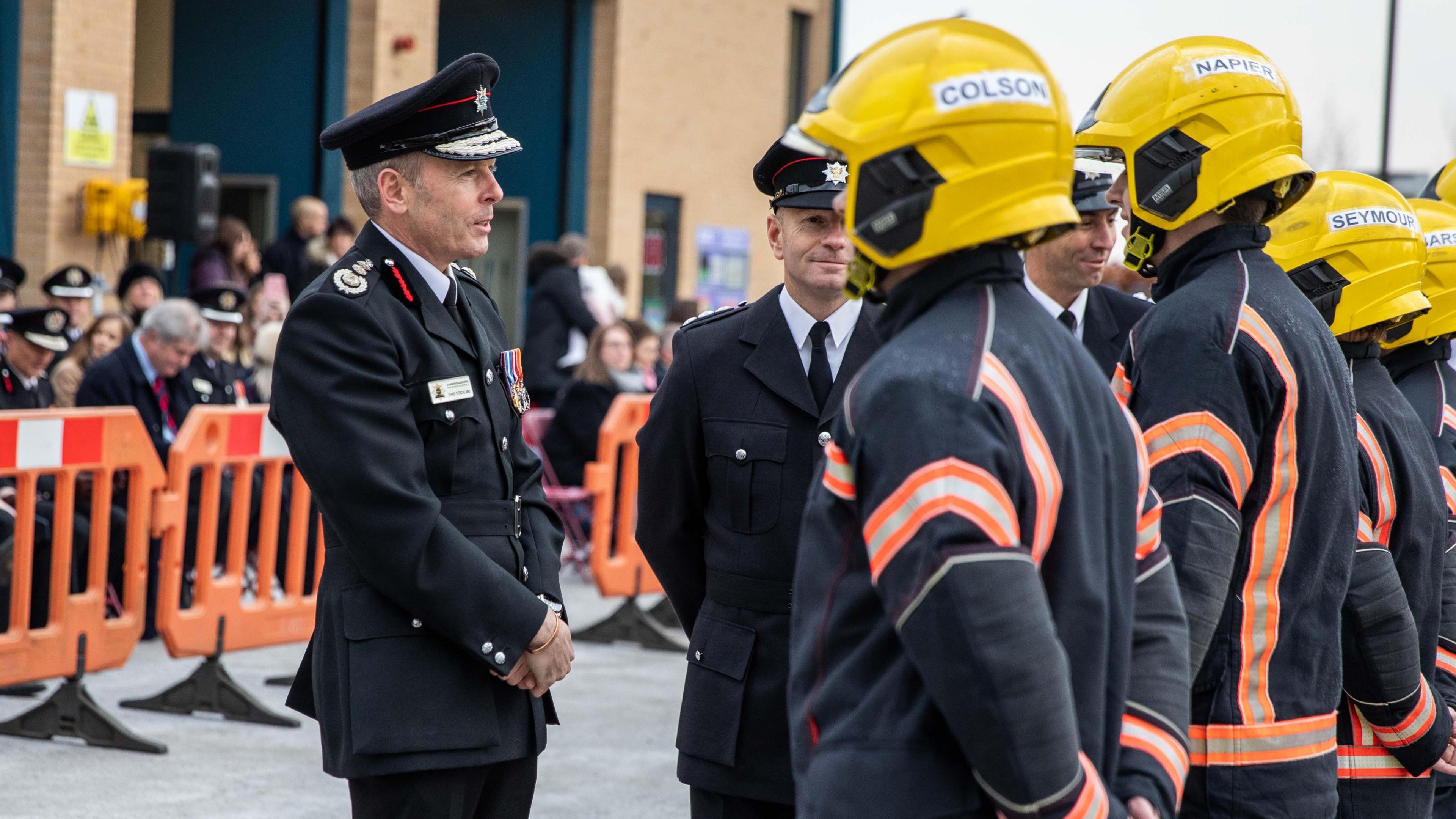 Chris Strickland in uniform stands in front of firefighters in uniform who are lined up to be inspected by him. 