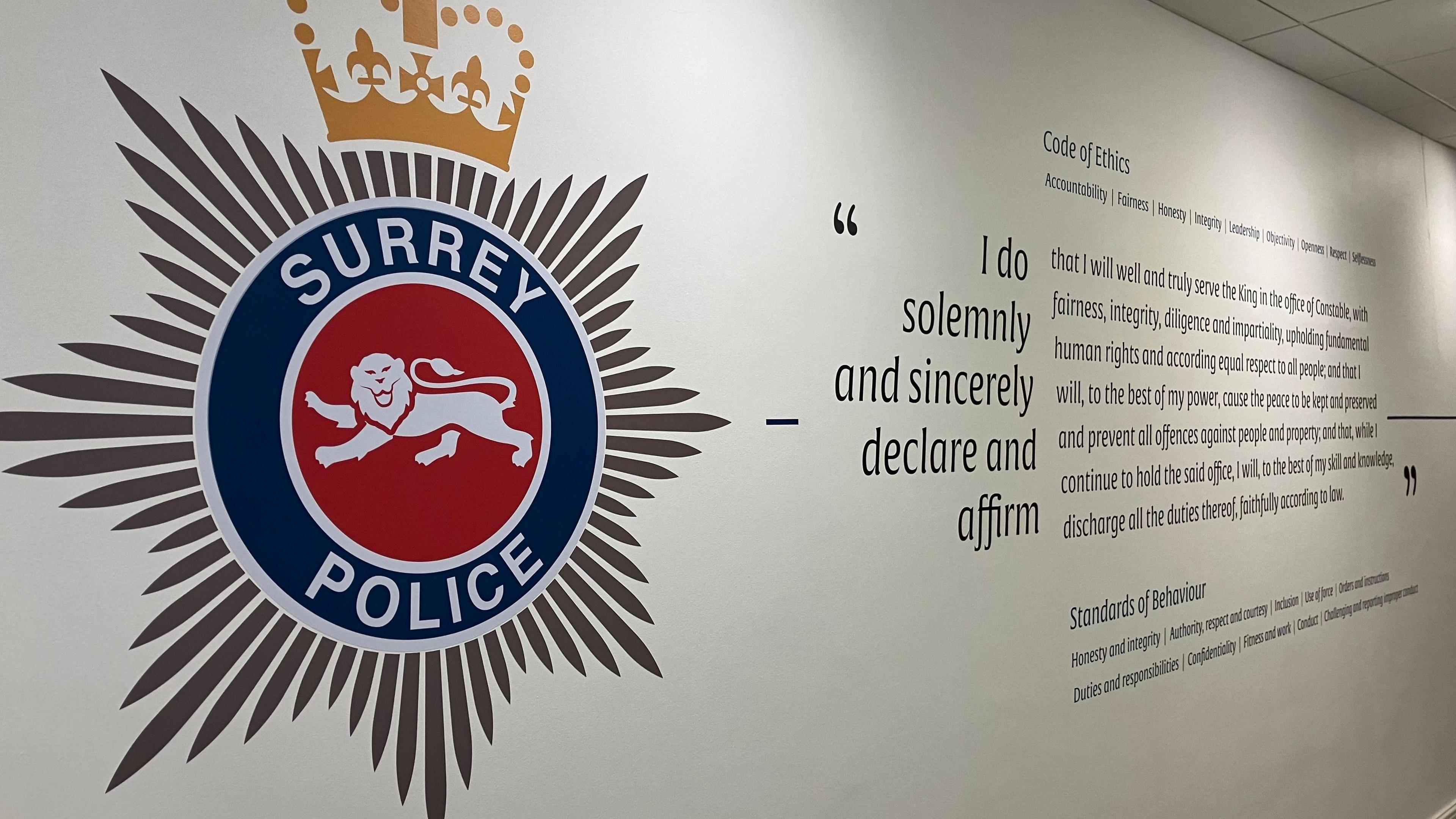 A white wall with the Surrey Police logo painted on. There is also a large amount of writing, reading: "I do solemnly and sincerely declare and affirm" the writing then gets small and details the force's standards of behaviour.