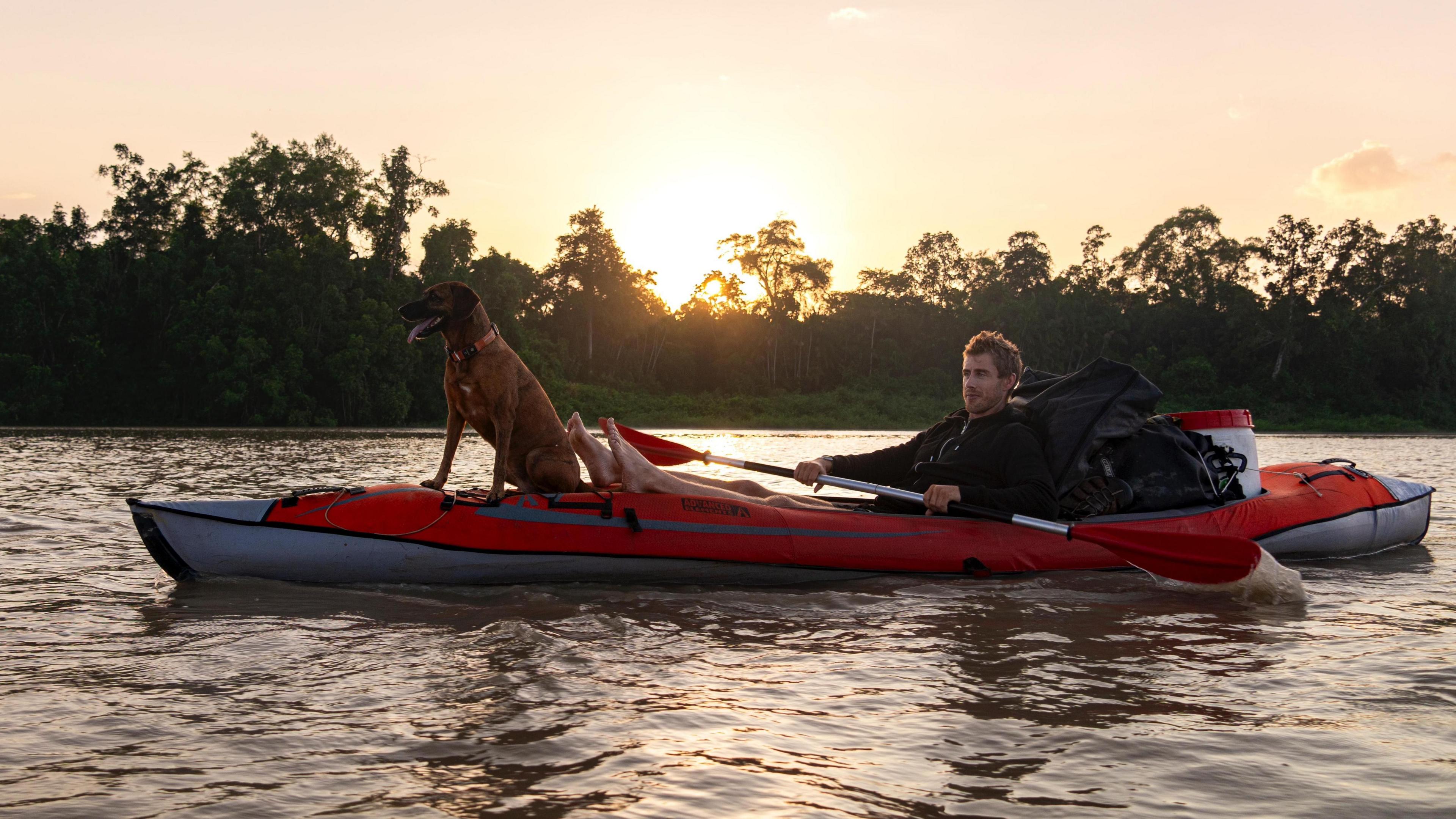 Ash Dykes in his kayak with his feet up and with the dog sitting at the front as the sun sets