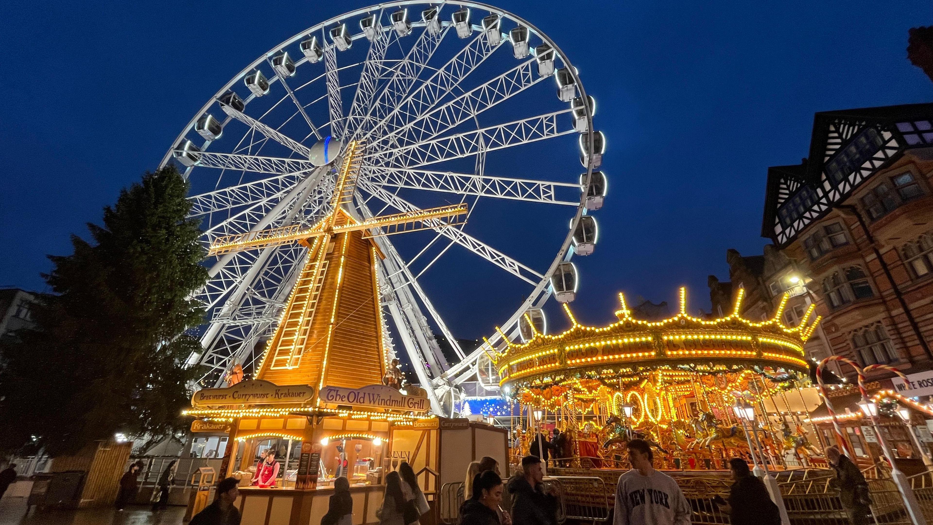 Giant wheel, stalls and carousel lit up at night