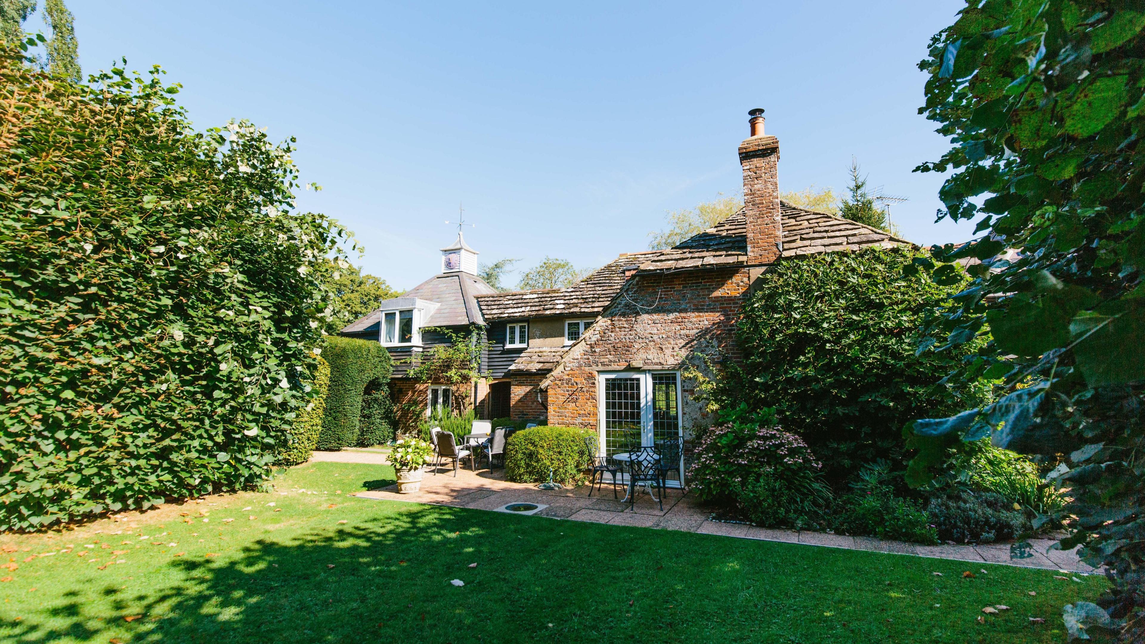 A brick cottage surrounded by hedges and other plants, with an immaculate lawn.