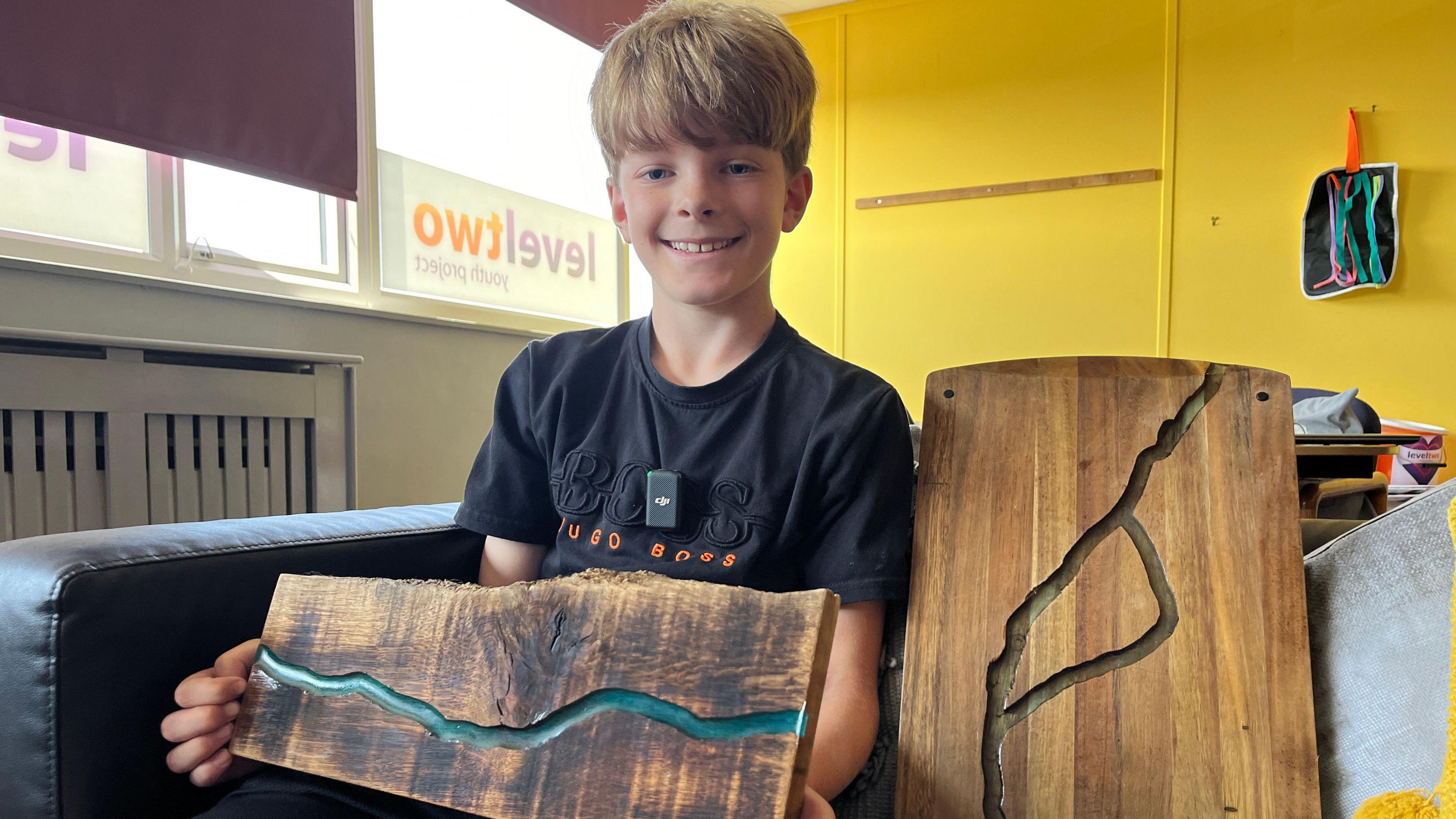 Oscar, 10, sits holding a wooden board with a blue resin filled groove across it.