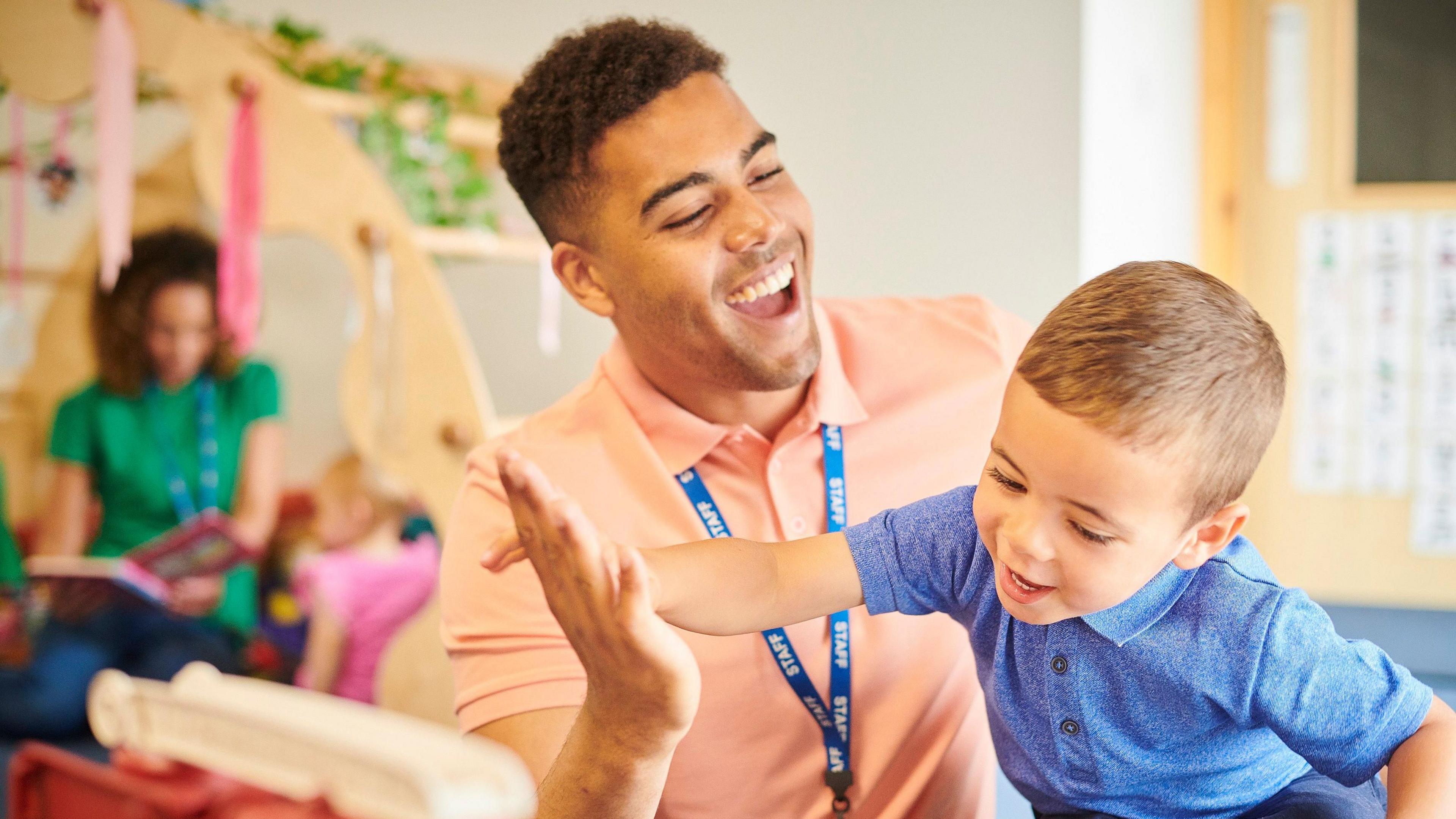 A nursery teacher high-fives a small child.