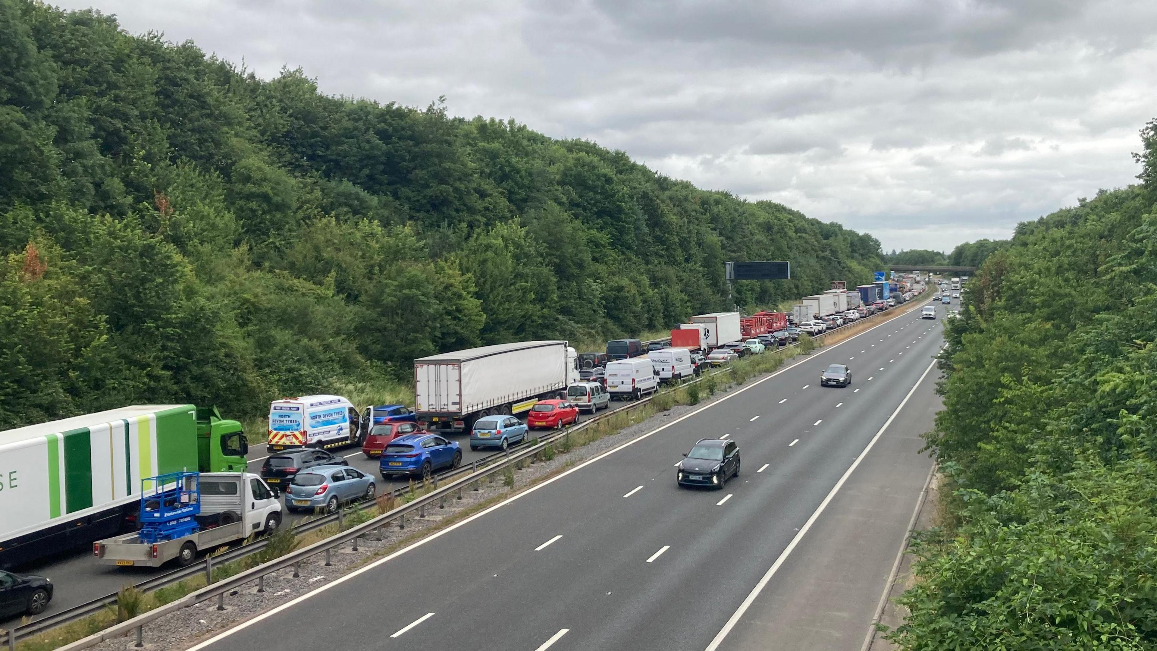 Queueing traffic including cars and lorries on the northbound side. Flowing traffic on the southbound side.