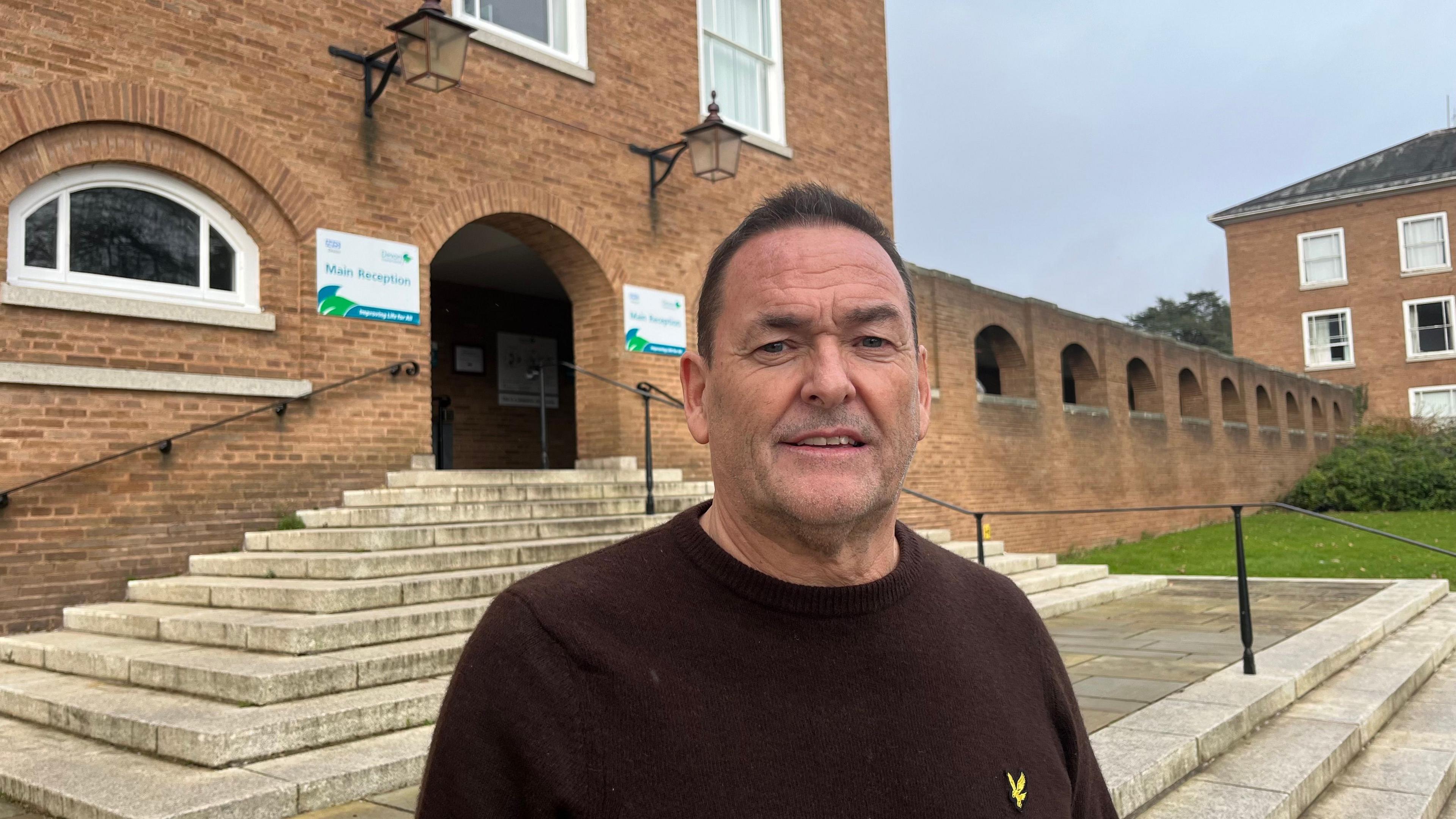 Ian Frankum, anti-LTN campaigner, wearing a brown jumper, at the front entrance to Devon County Council offices