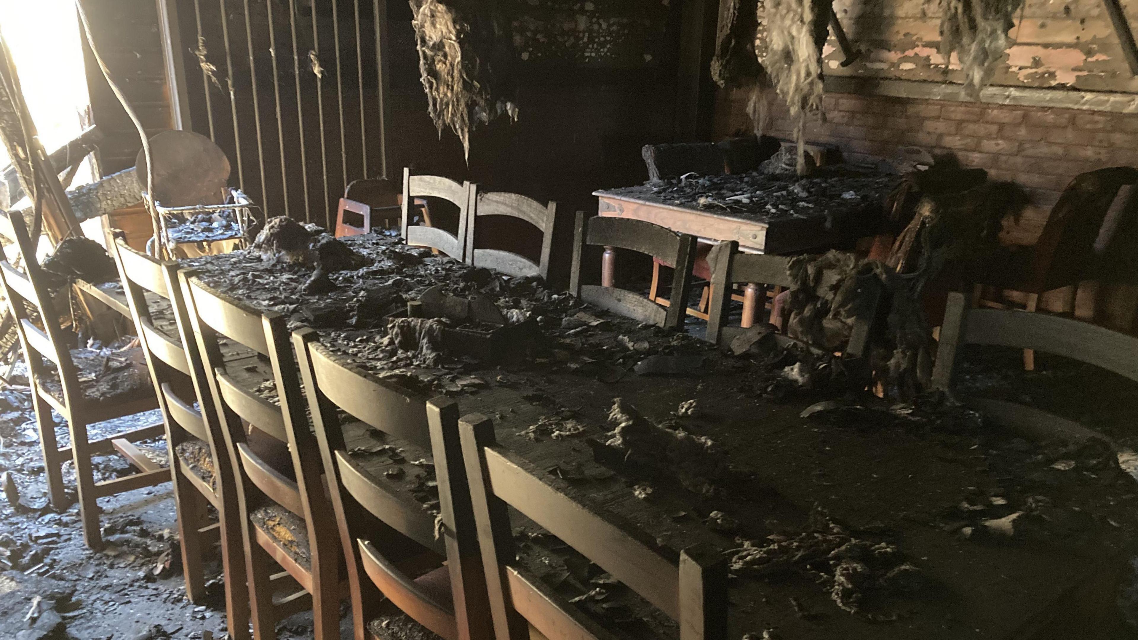 A table which is covered in ash, below the roof which has debris hanging off it.