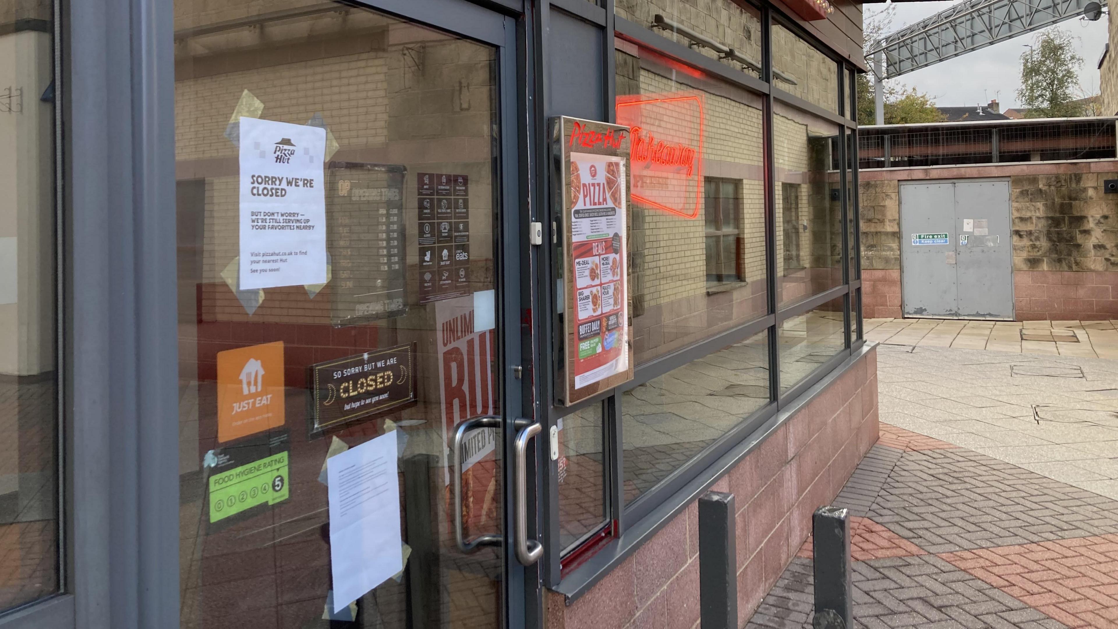 The front door of a restaurant, with numerous signs stuck to it. Some of them indicate it is closed.