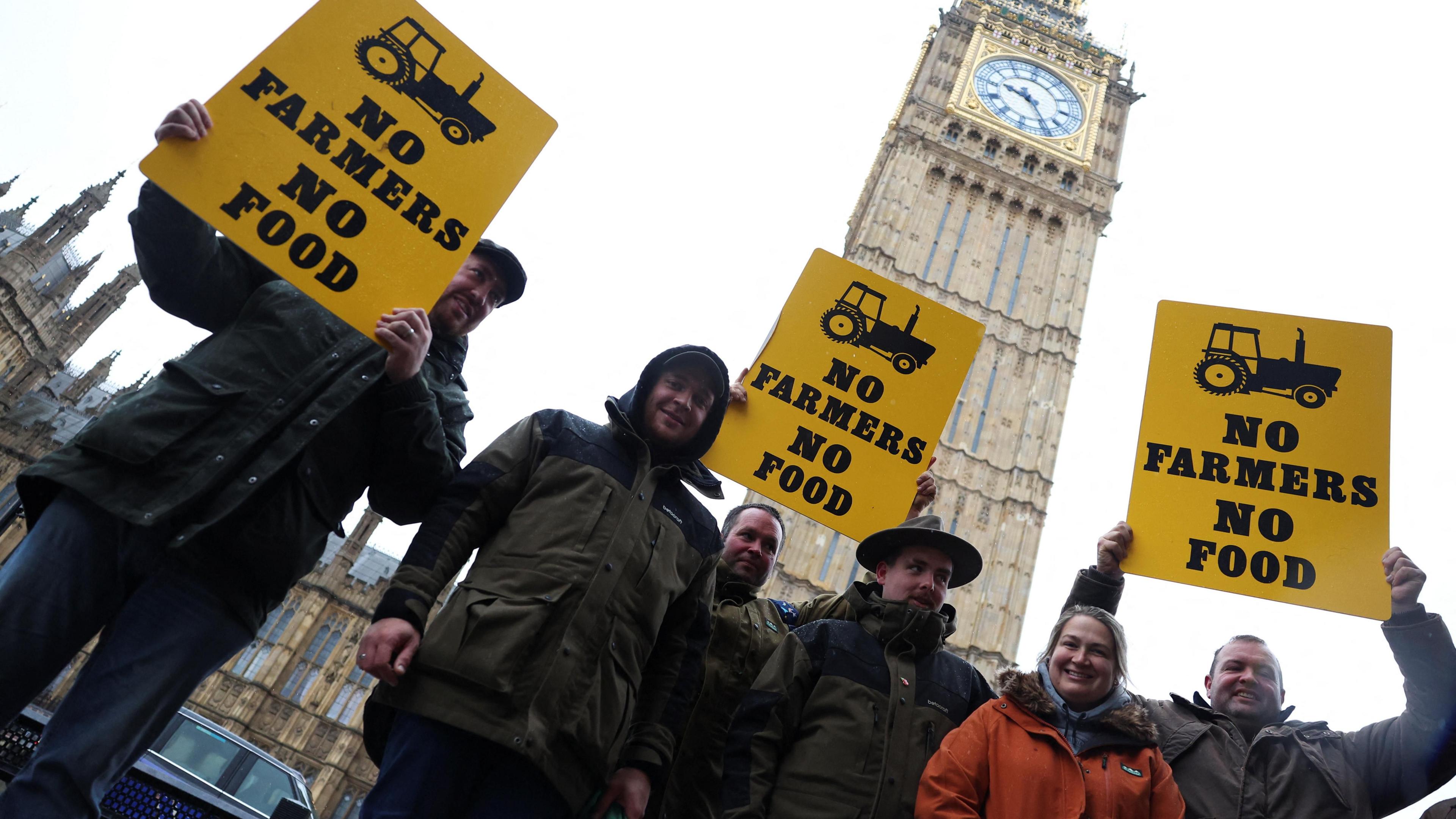 A group of farmers holding yellow signs that say 'no farmers no food' in black stand outside Big Ben. 