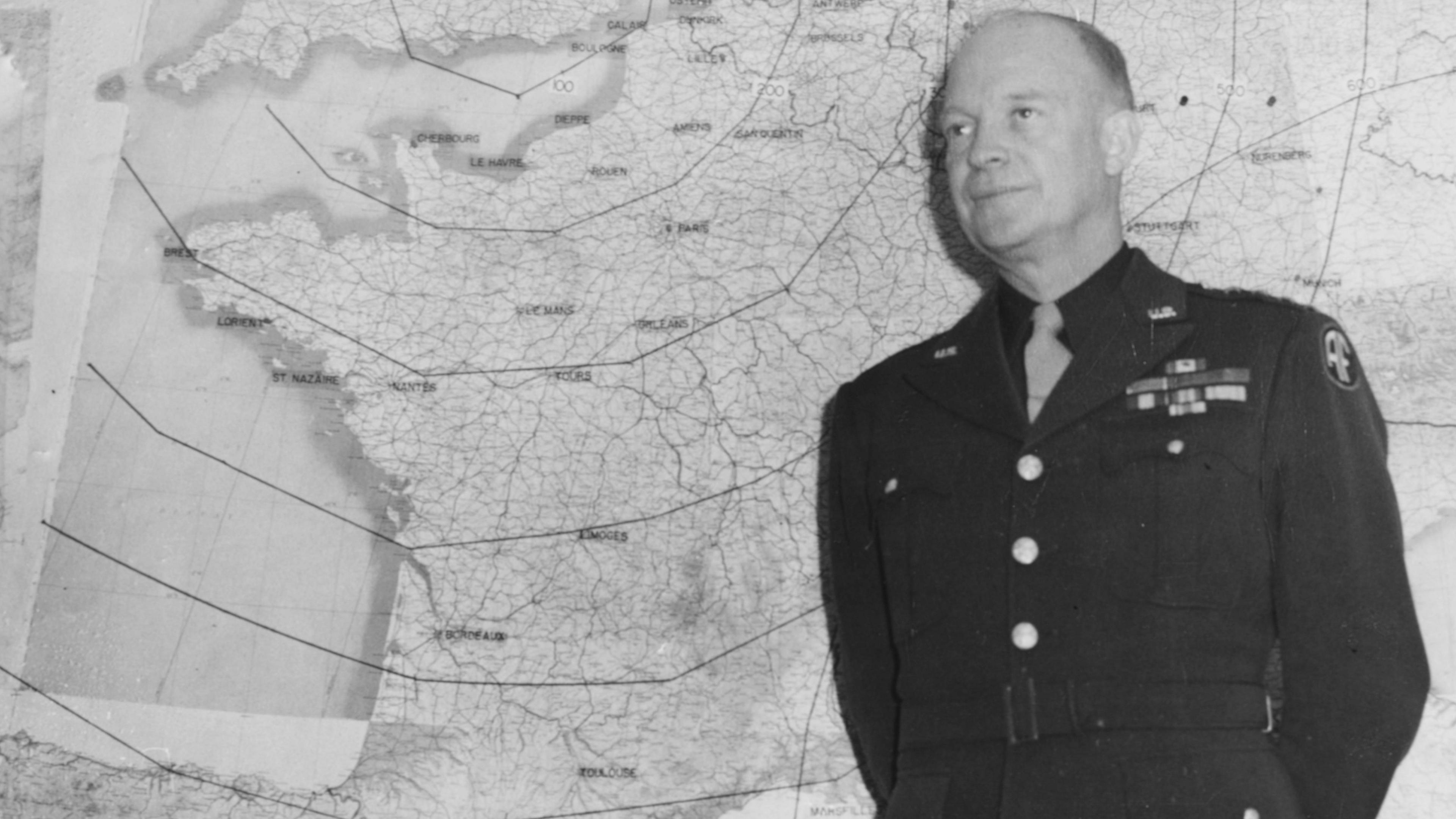 Black and white photo of man in military uniform, standing in front of a map of France