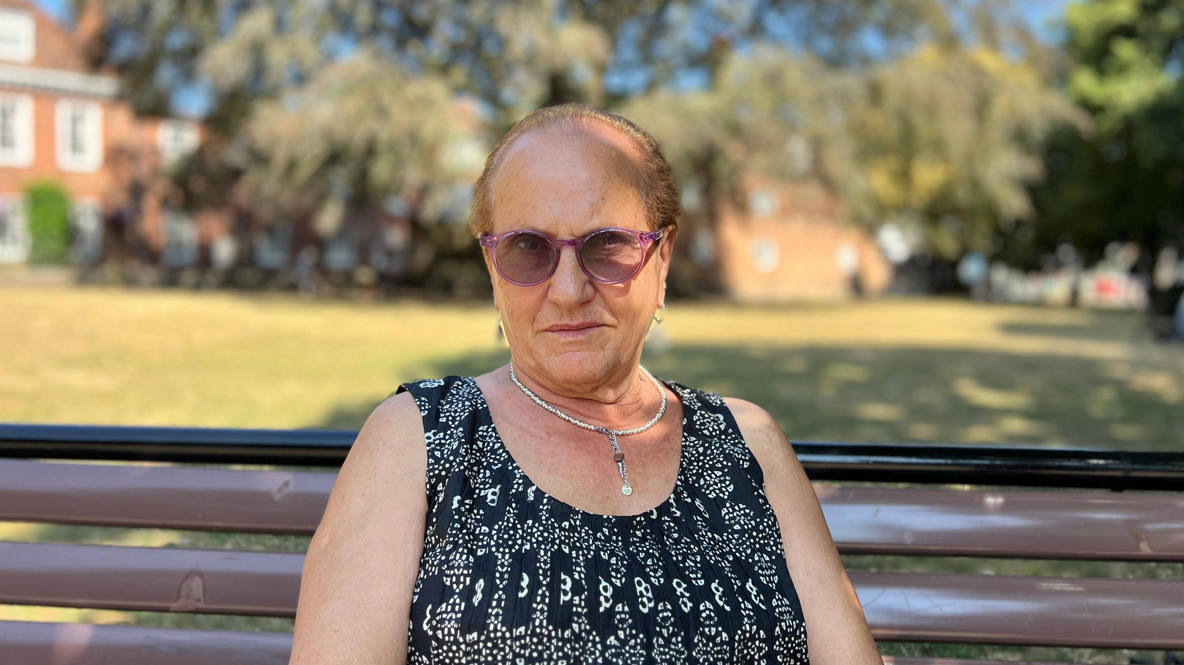 Anna Maretlli is wearing a black and white dress and a silver necklace, she has purple rimmed sunglasses and is looking directly at the camera.