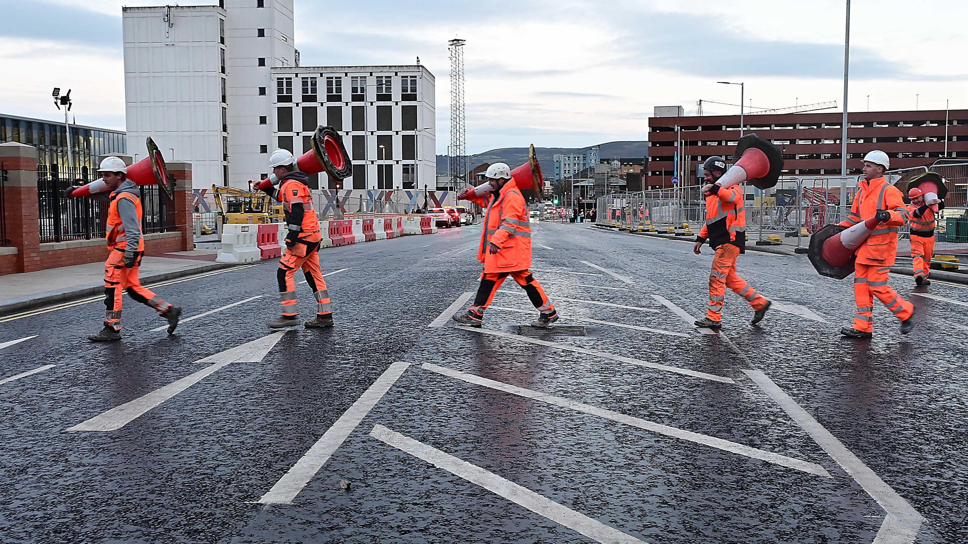 A group of people wearing orange high visibility clothes moving bollards off the road. 