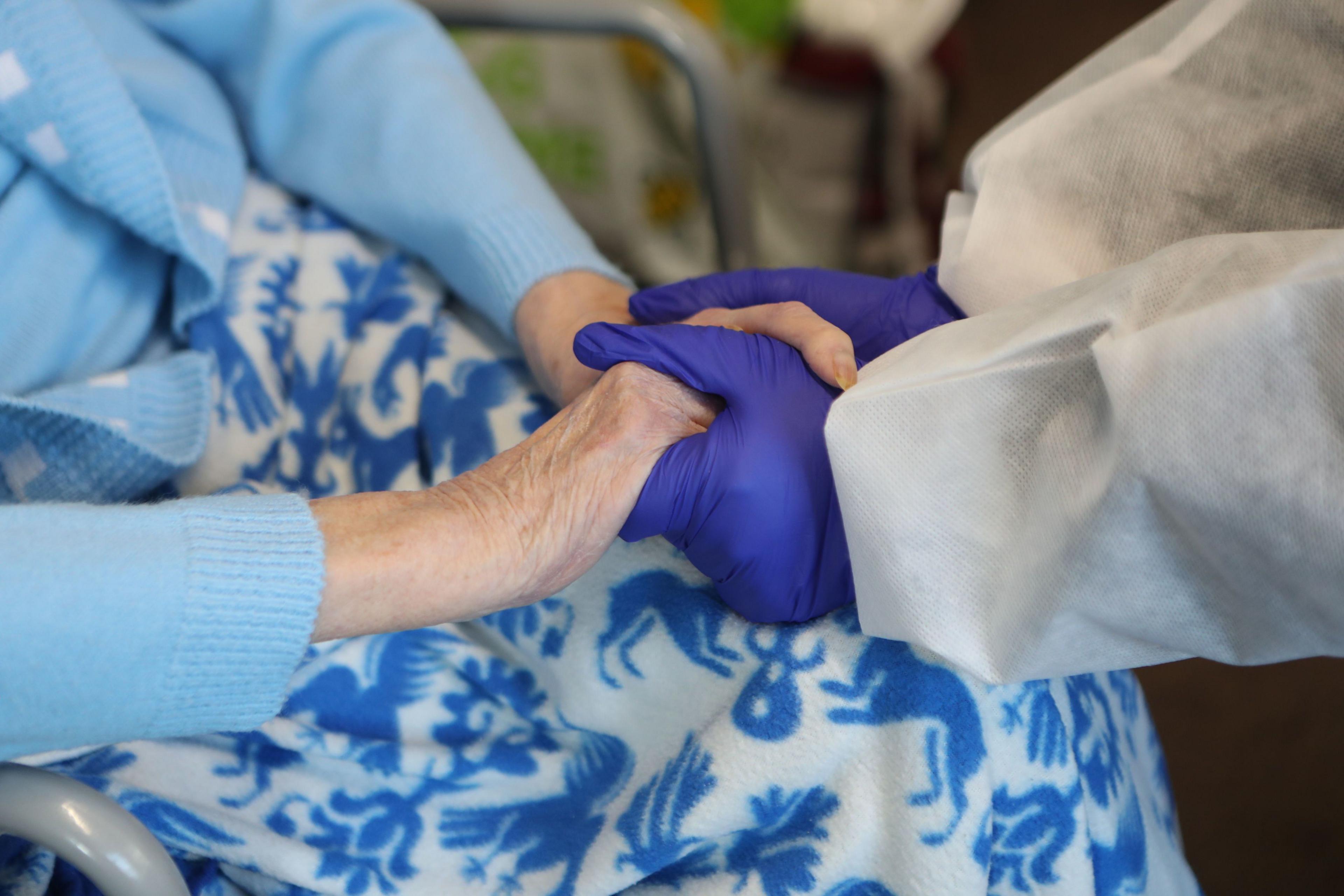 Old person having her hand held by a nurse