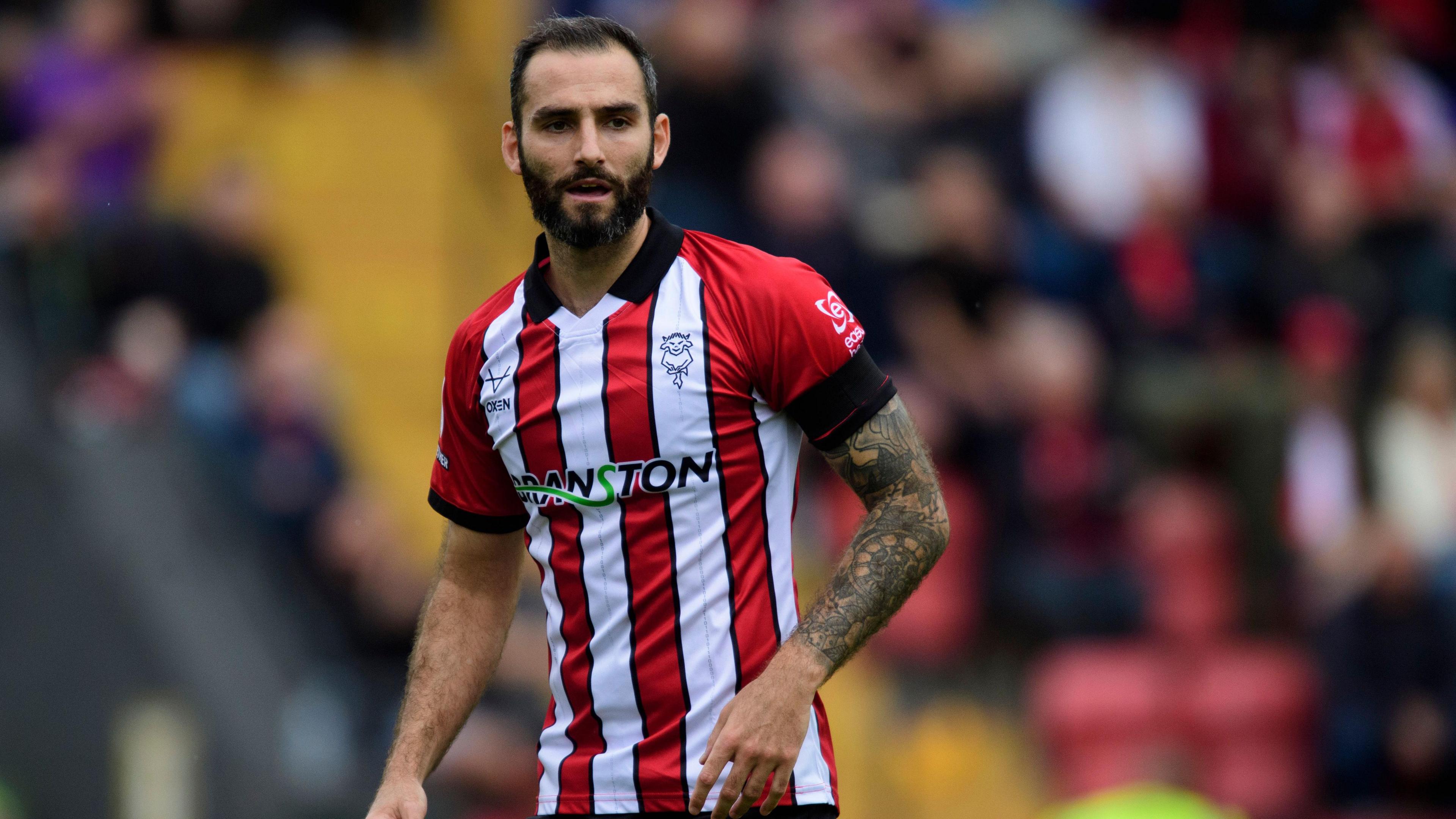 Adam Jackson plays for Lincoln City in their red and white striped home kit during a match against Mansfield Town in August 2025