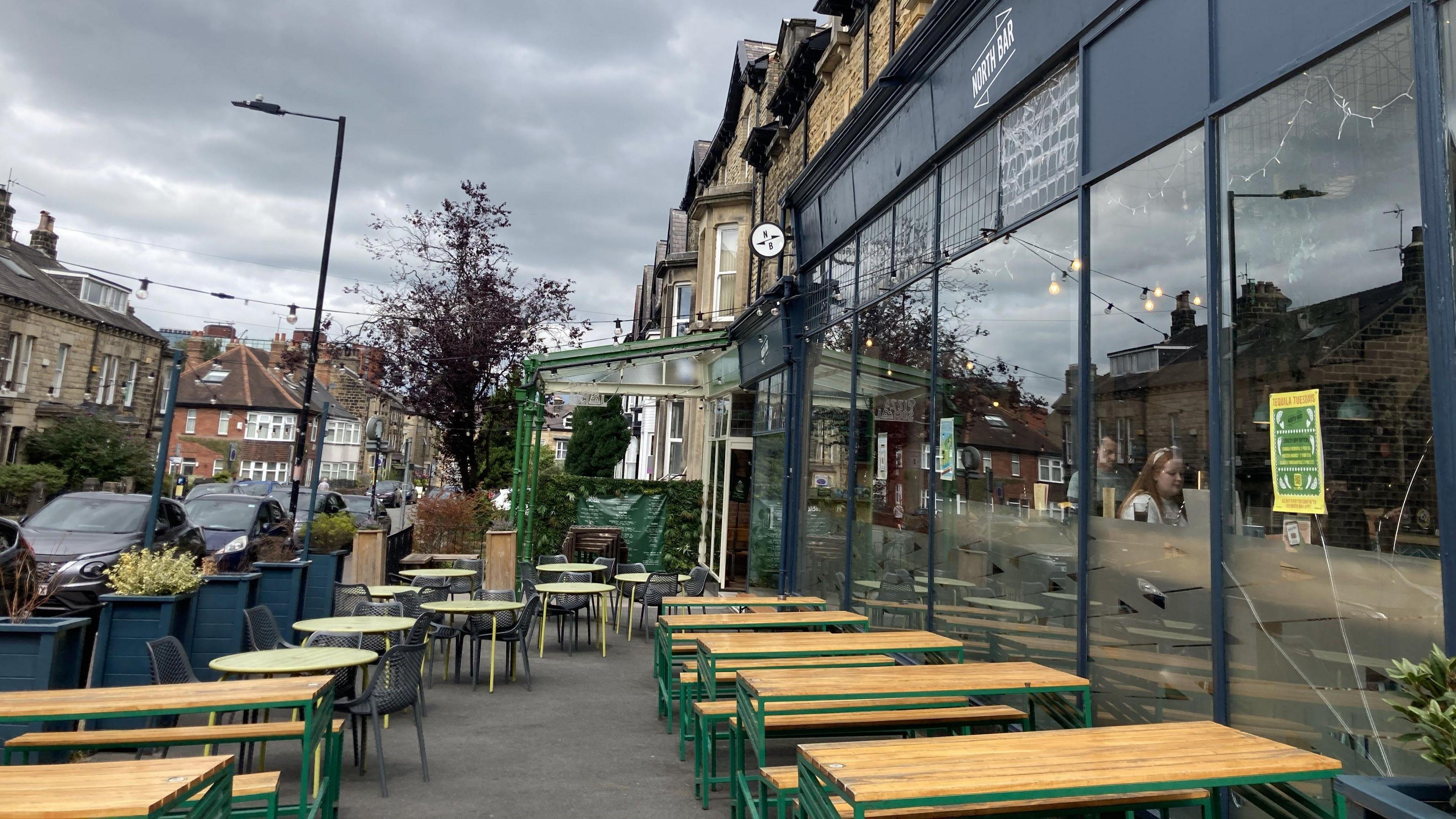 The outdoor seating area at North Bar in Harrogate, with long wooden tables and green metal benches.
