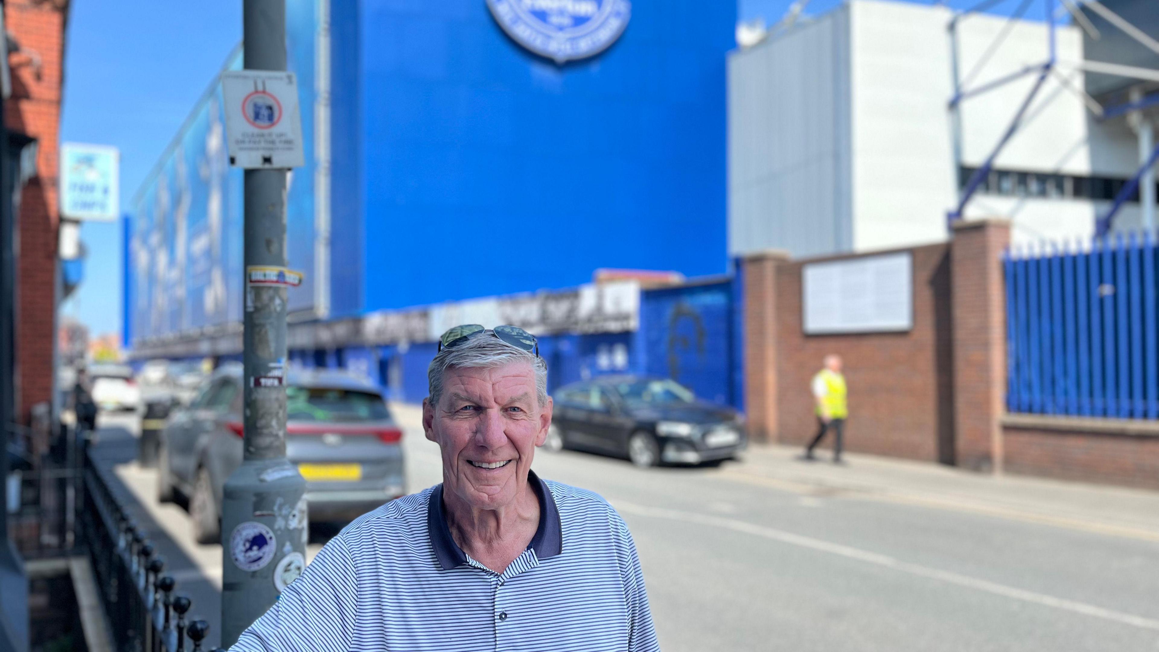 Ray Parr is standing in front of 9 Goodison Road and smiling directly in the camera. Behind him in the background is Goodison Park.