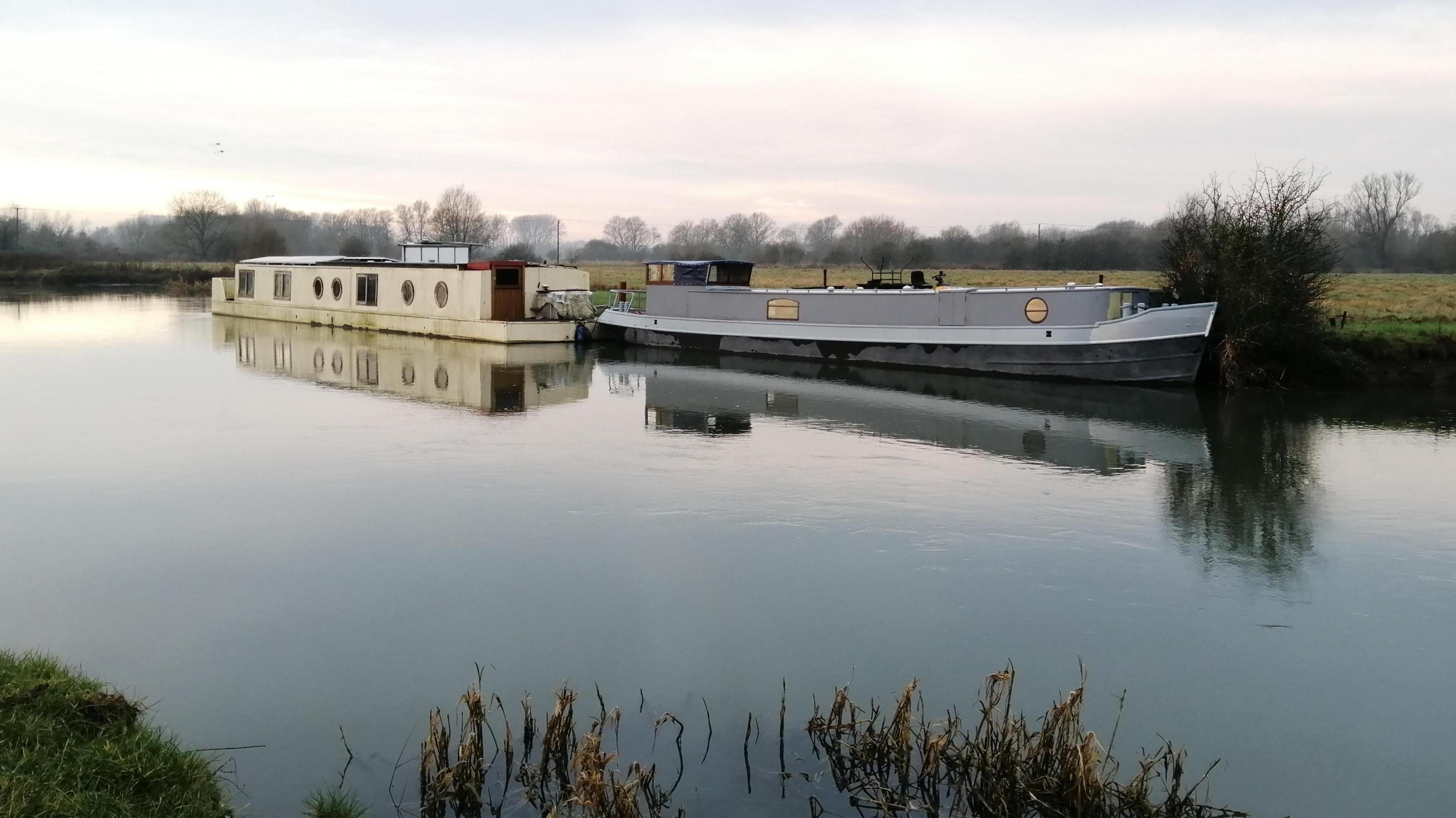 Two boats on very still water with a grey sky in the background.