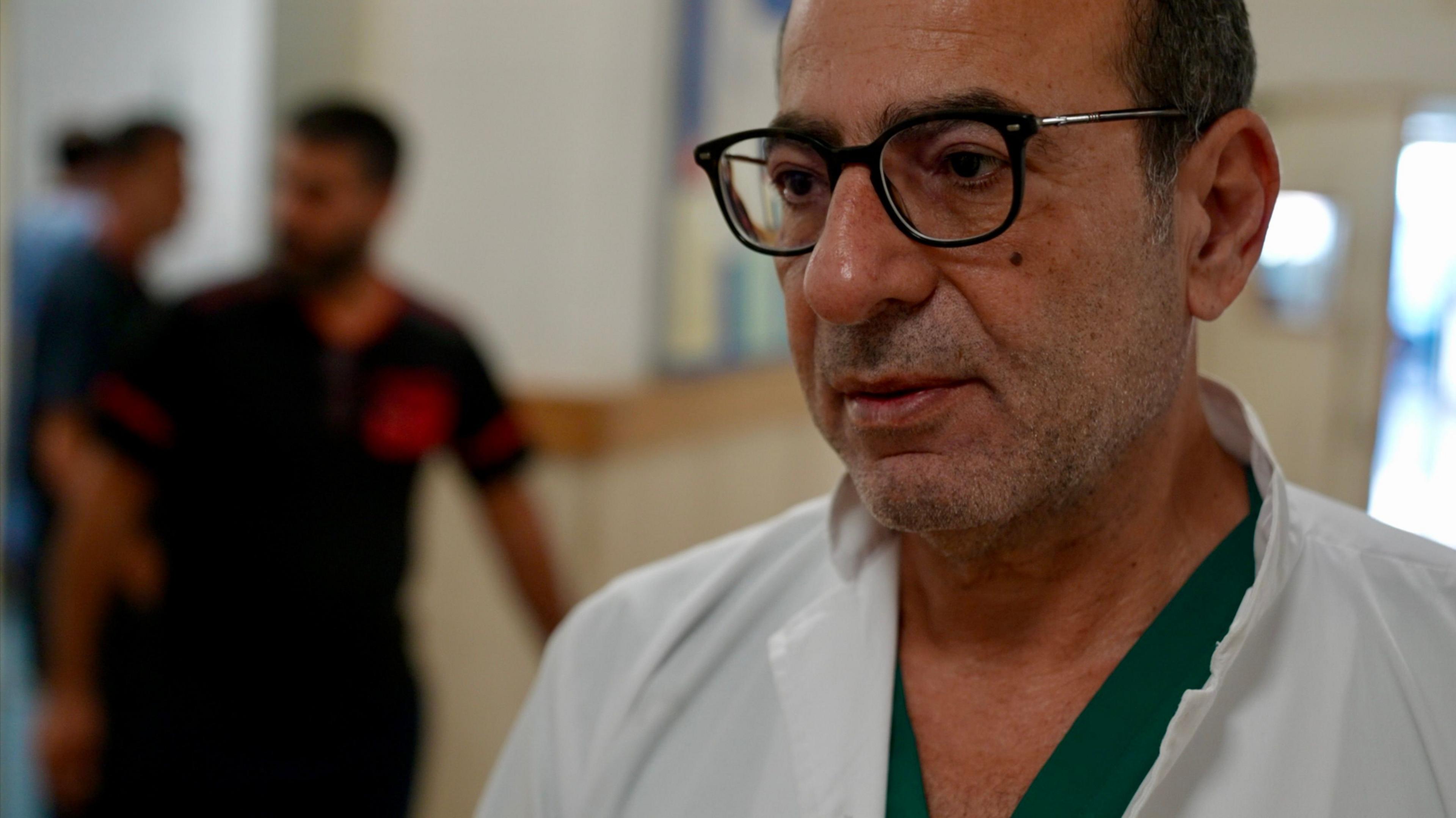 Dr Hassan Wazni pictured in the Nabih Berri government hospital. He is a middle-aged man in a white doctor's coat, green scrubs and dark-rimmed glasses.