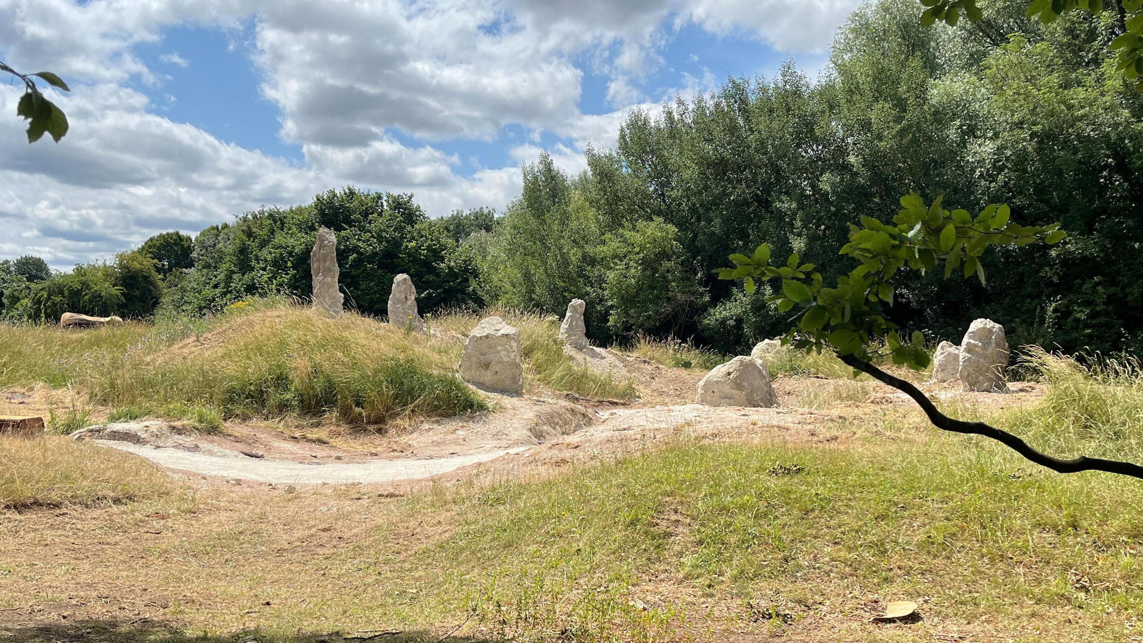 Eight chalk stones form a circle as part of a new henge. There are trees in the background and the stones are surrounded by wispy grass.