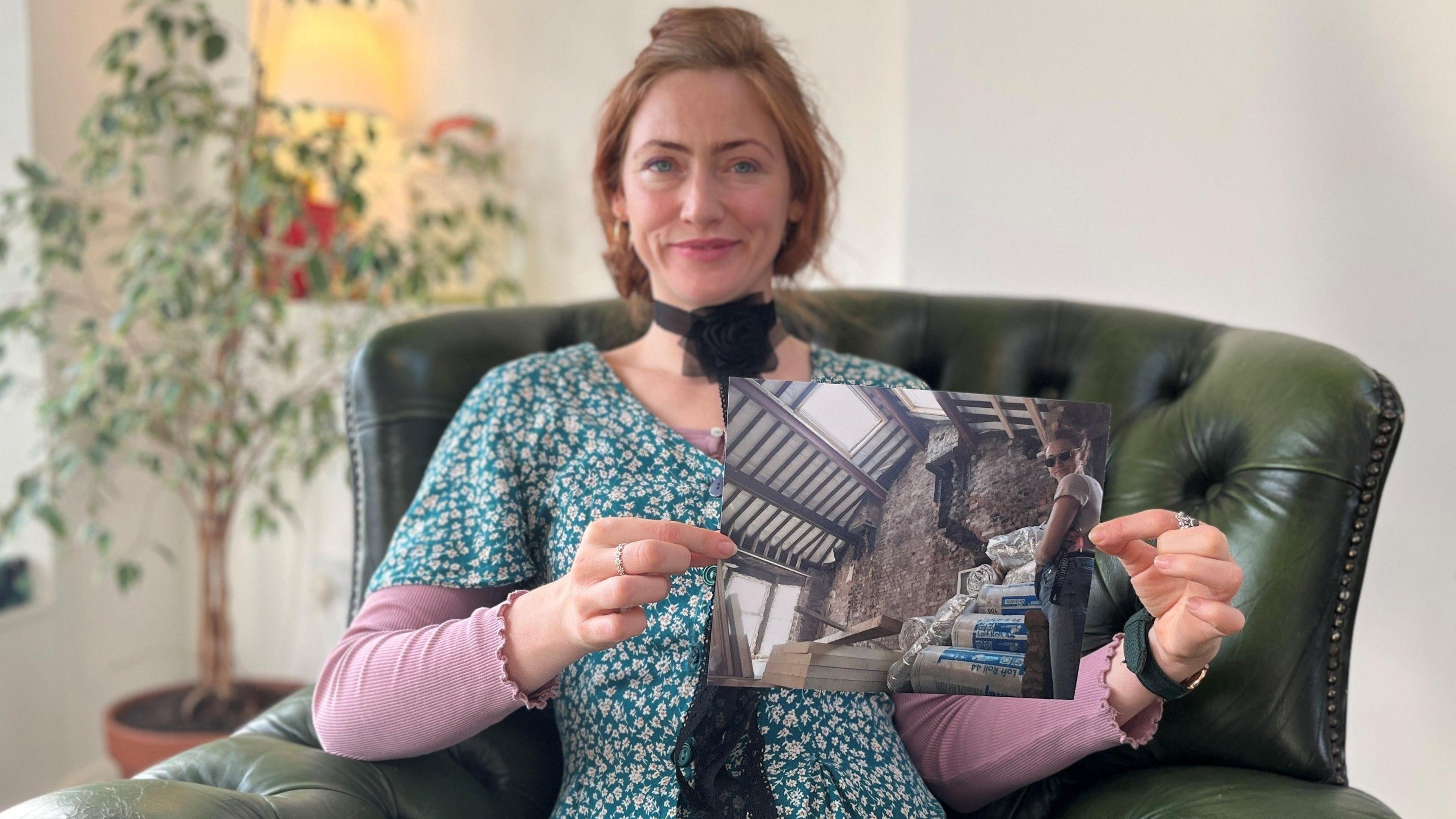 Maxine Sharples sitting on a sofa and holding up a photo.