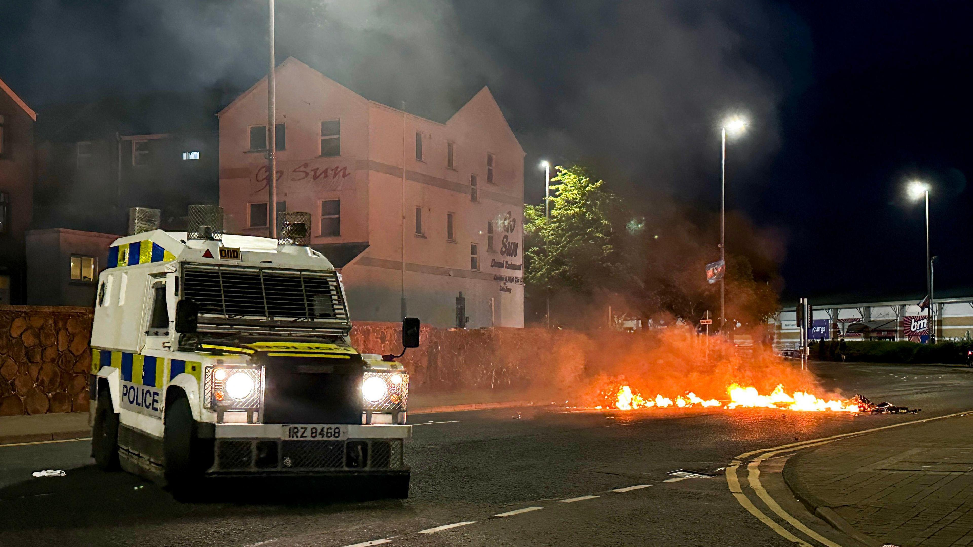 A PSNI vehicle parked on a road, with debris set on right to the right of it.
