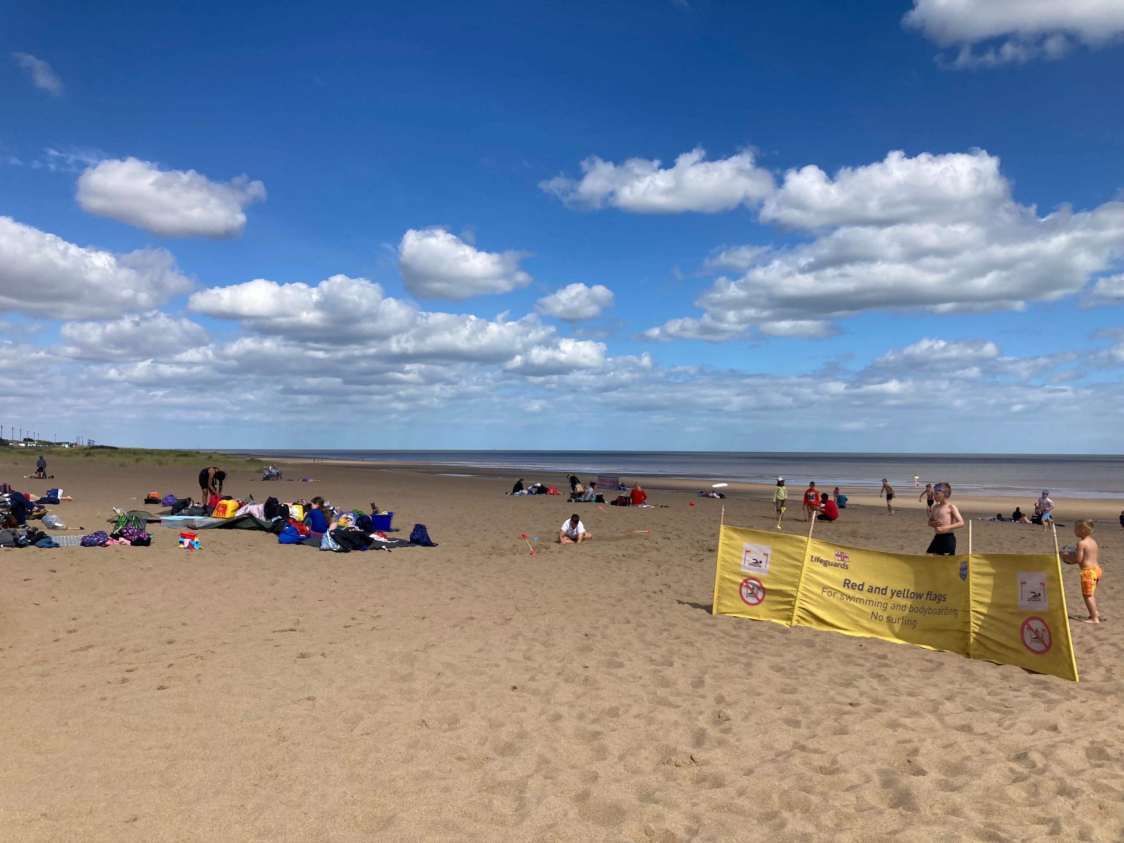 Families can be seen enjoying a day out on the beach, which has golden sands and the sea in the distance.