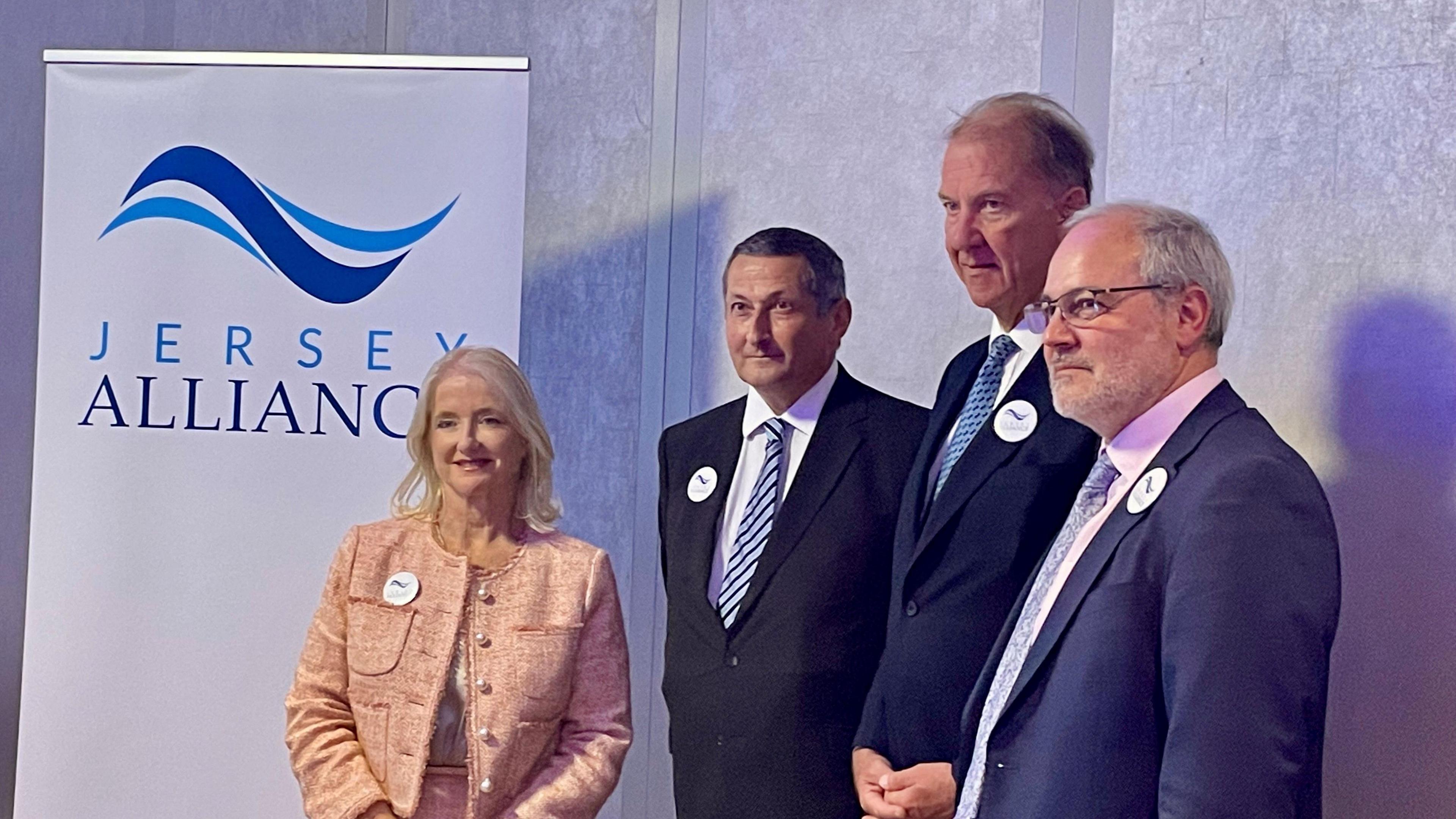 From left to right, Mary O’Keefe, Lyndsay Ash, Rowland Huelin, Gregory Guida. The woman on the left is stood in front of a white and blue sign which has the words JERSEY ALLIANCE. 