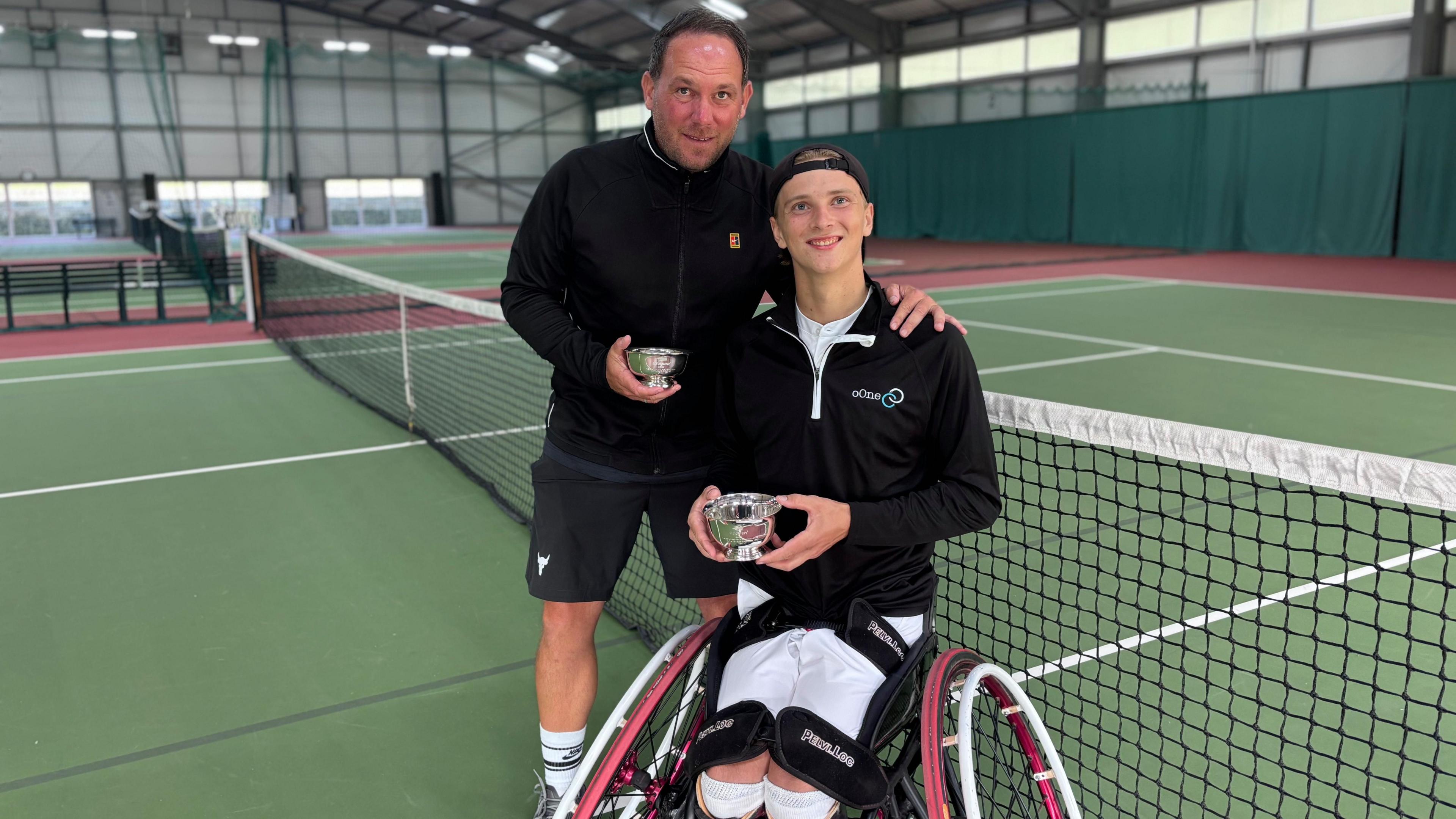 Ruben Harris and his coach Robert Fullagar at Canterbury Tennis Club holding US Open trophies, which are awarded to coaches as well as competitors