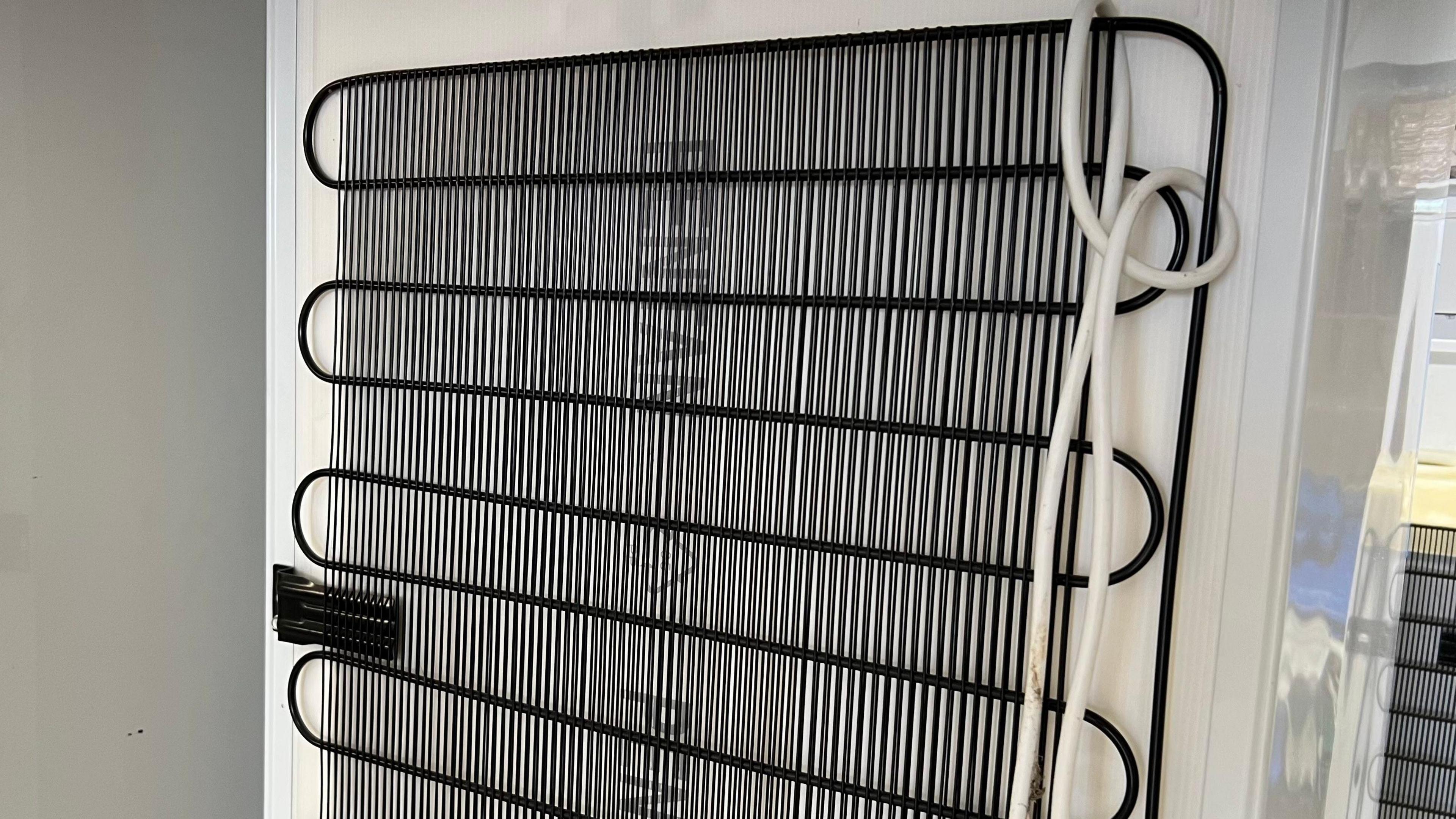 The back of a fridge showing the black coils and vertical strips of the refrigeration system.