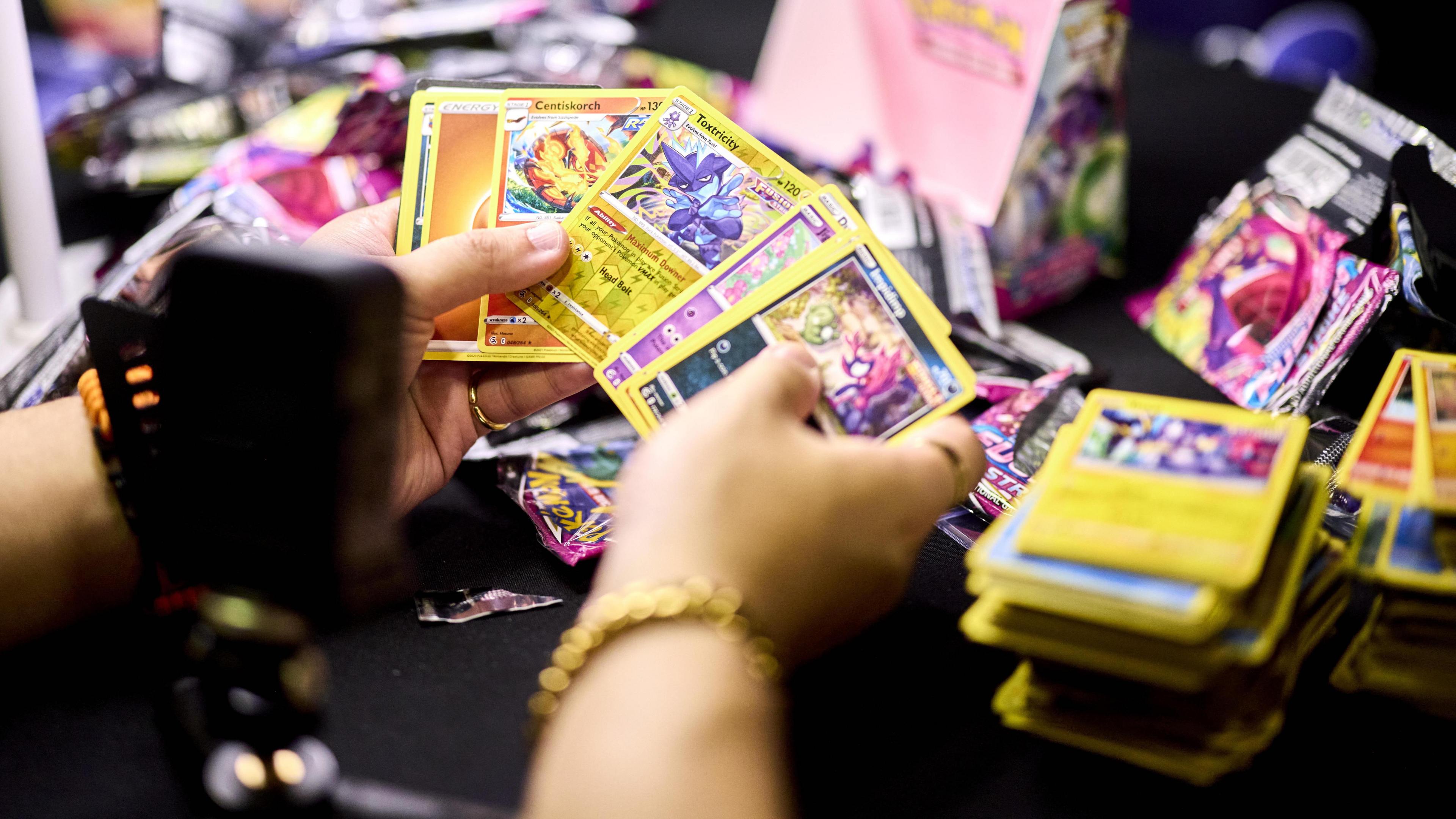 Two hands holding multi-coloured Pokemon cards in front of a camera.