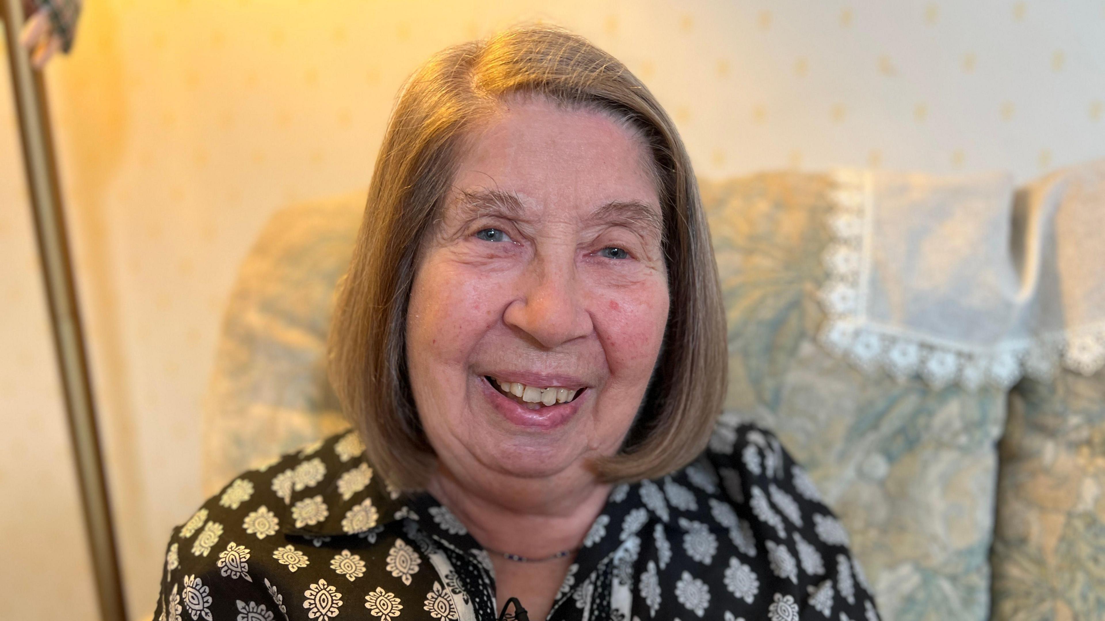 Maggie smiling on a sofa in her Cambridge home.