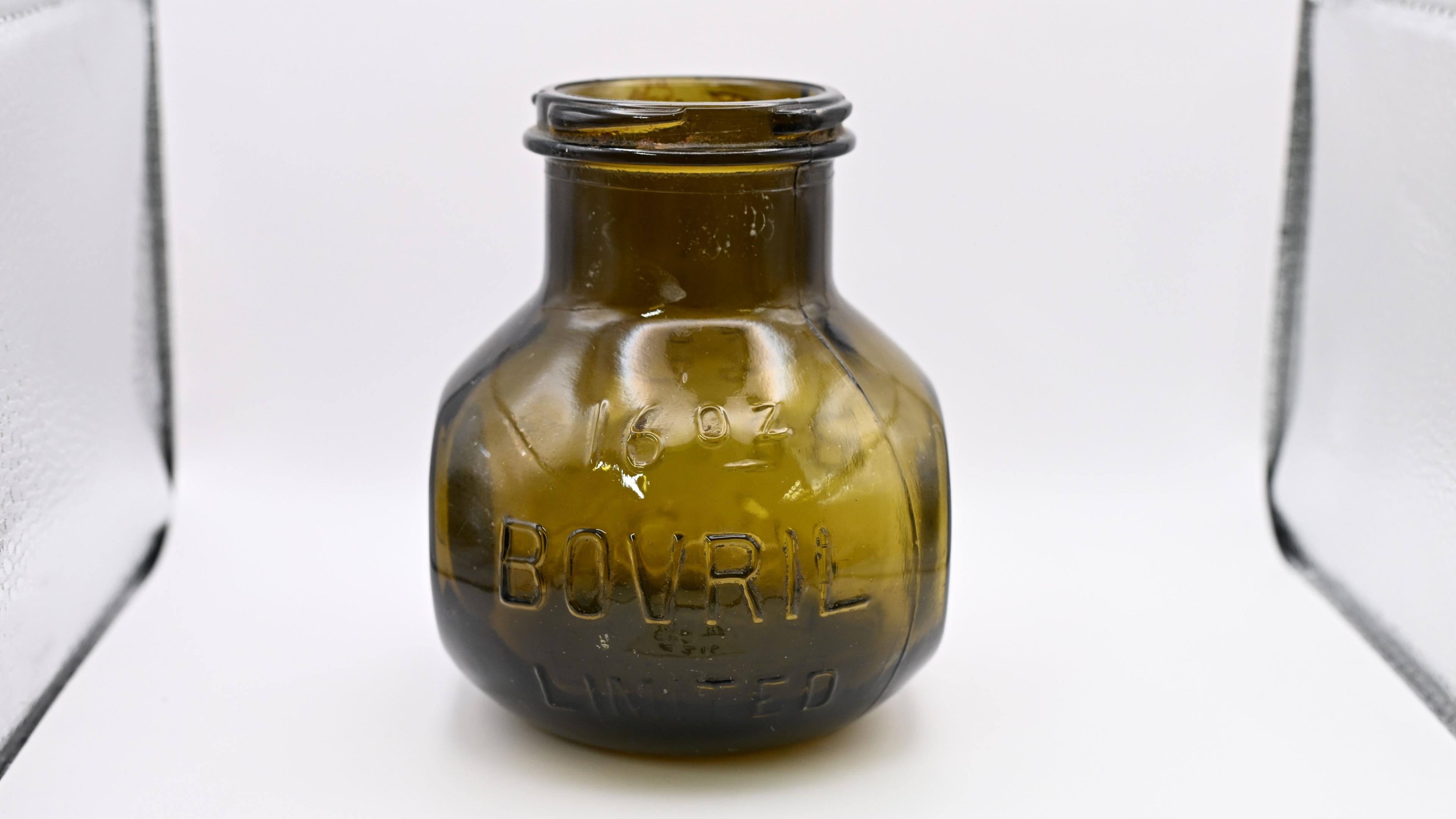 A historic jar in a white display cabinet. It is brown.