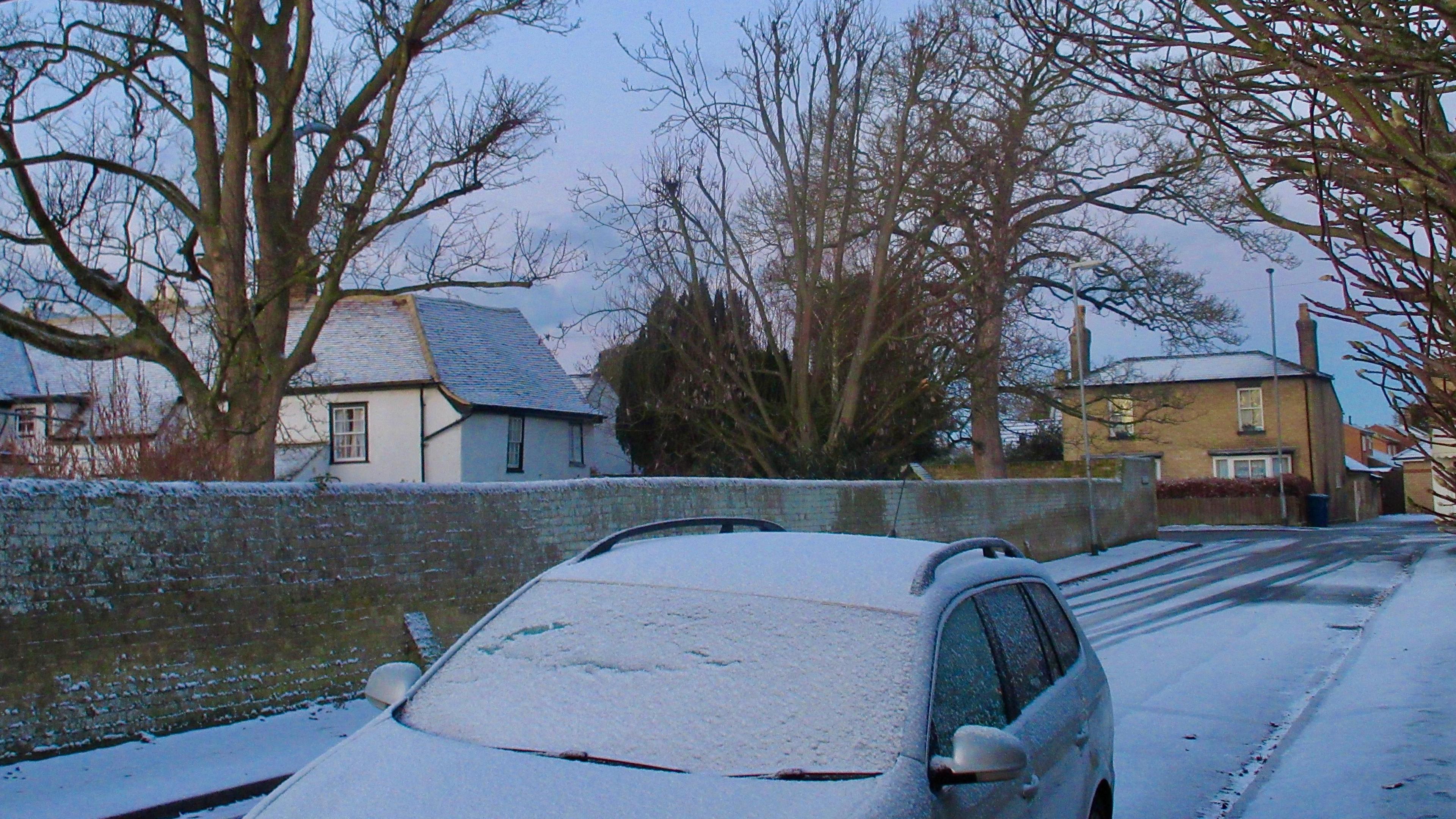 Snow coated car, road and rooftops on a residential street